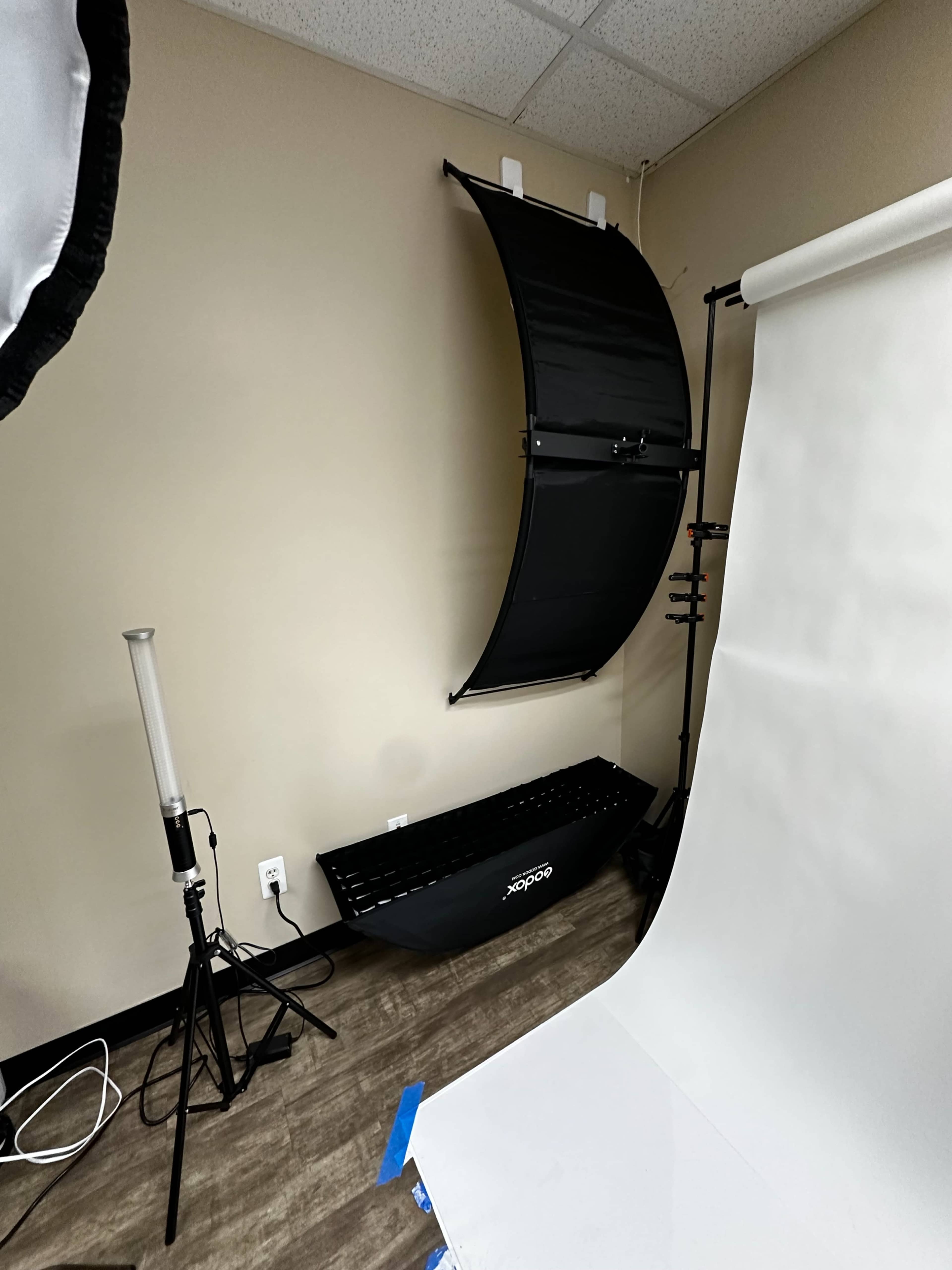 A photography studio setup with a curved backdrop, a lighting stand, and a white seamless paper roll.