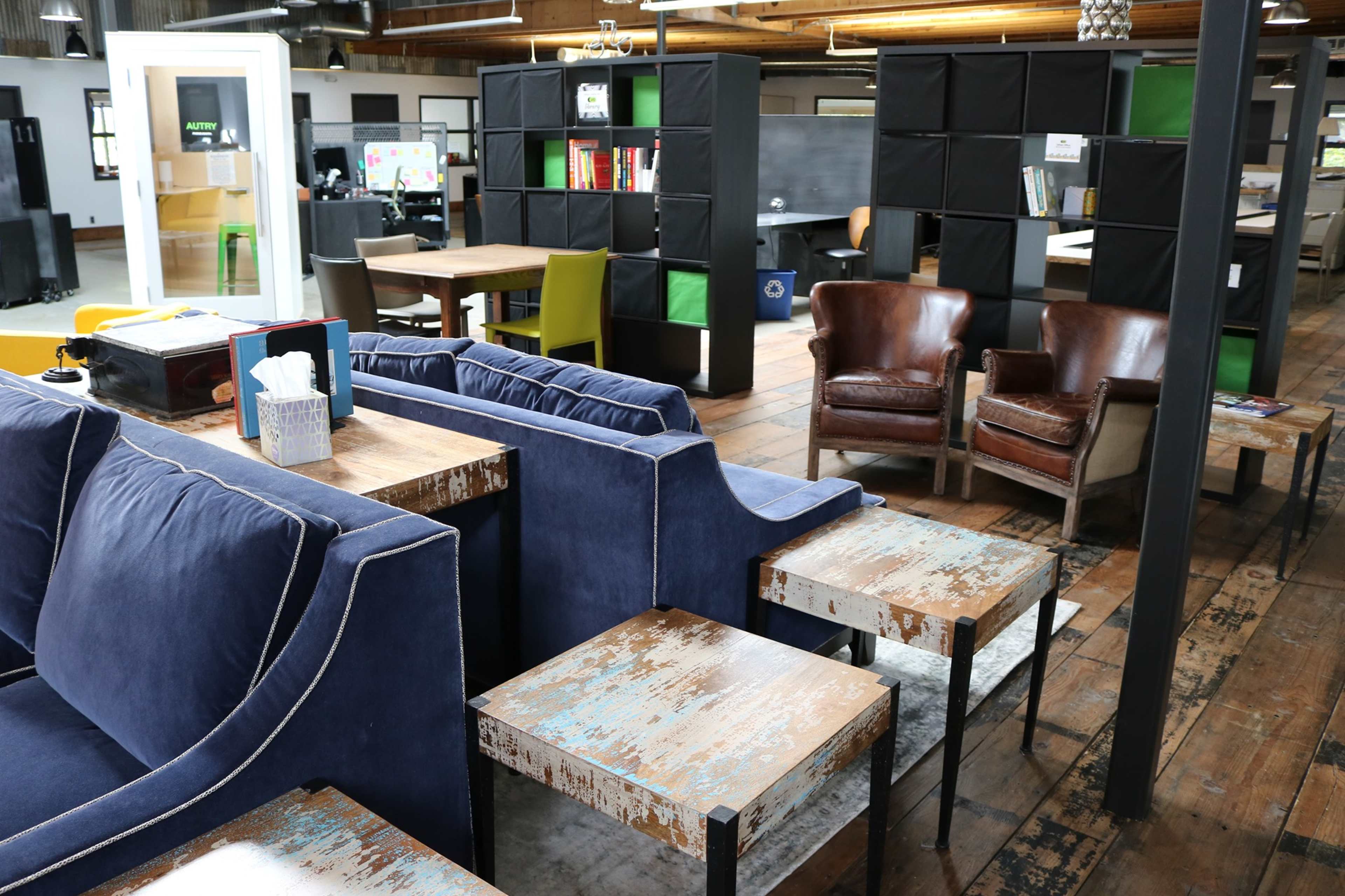 A modern office space with blue sofas, wooden tables, and a mix of seating arrangements including brown leather armchairs.