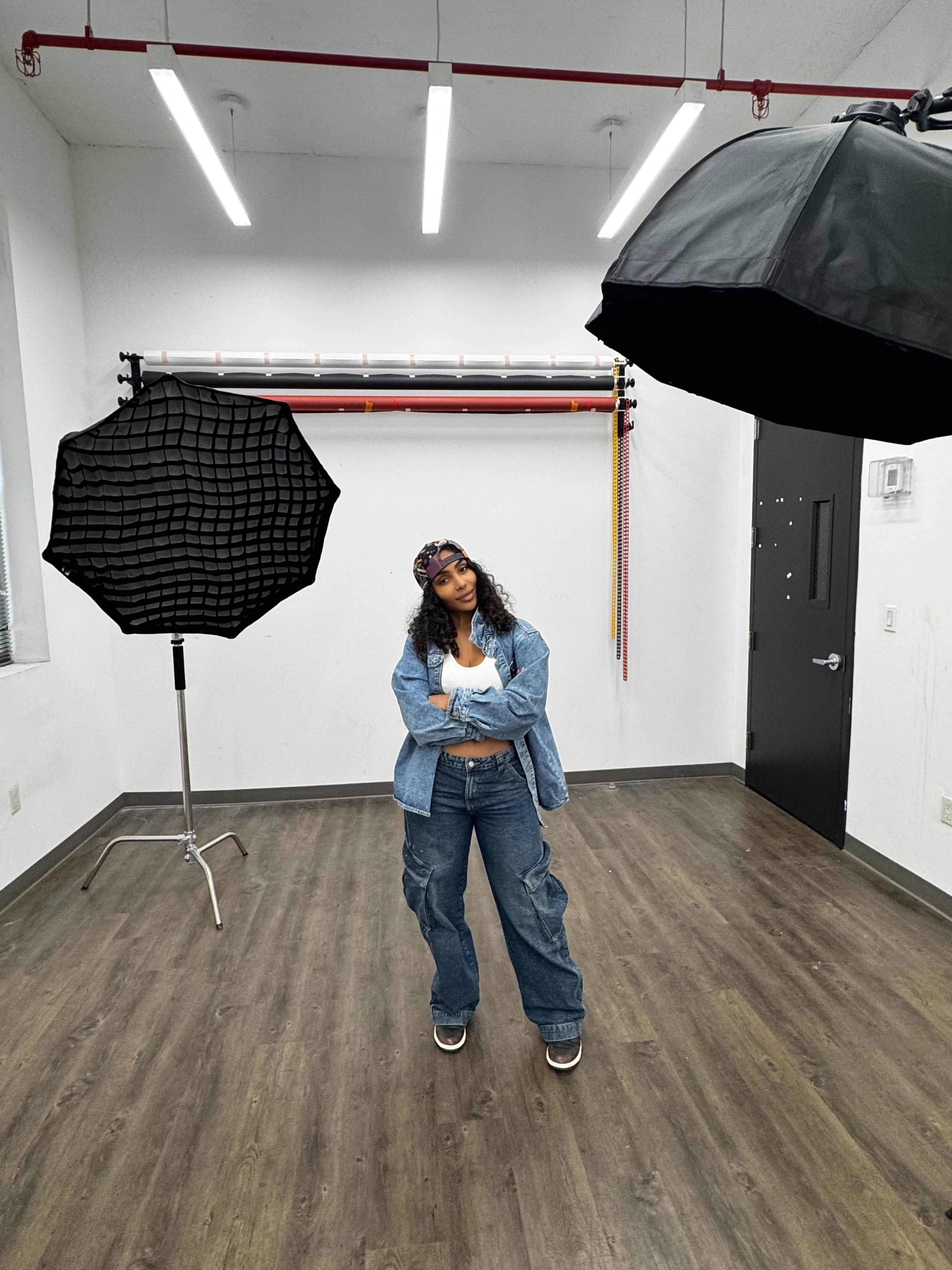 A person stands confidently in a photo studio, surrounded by studio lights and backdrops.