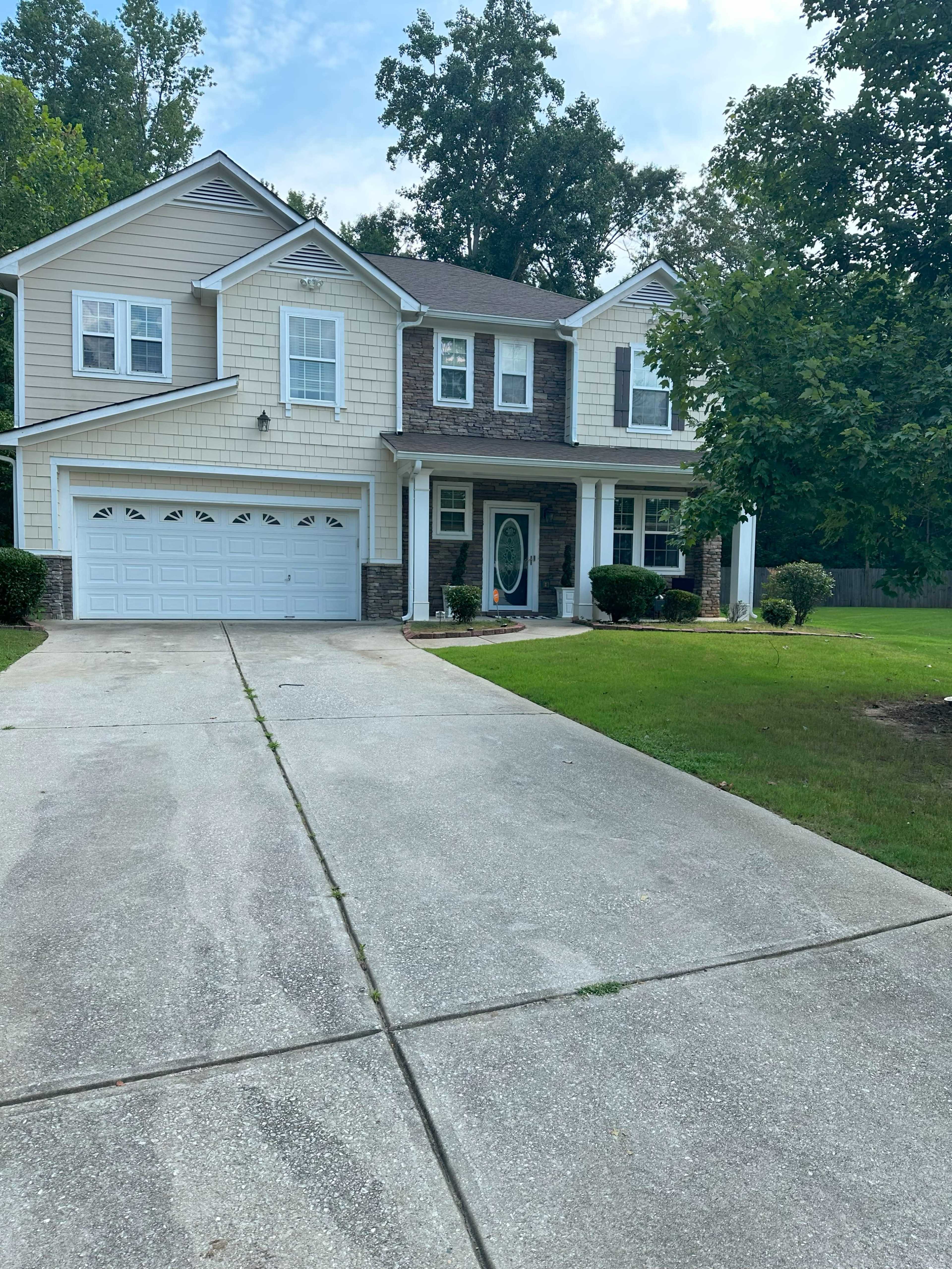 A two-story house with a stone and siding exterior, a front porch, and a driveway lined with grass.