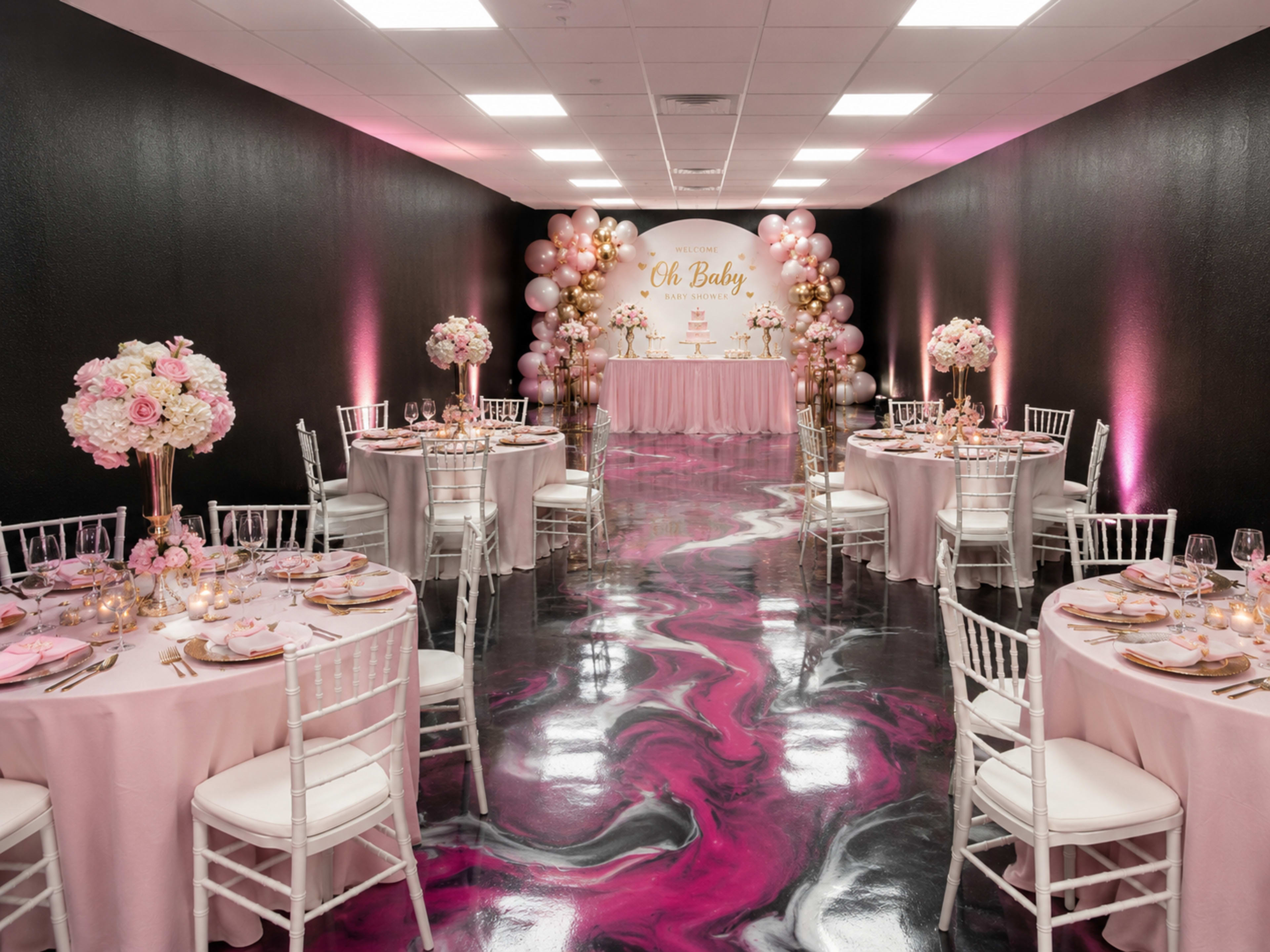 The image shows a decorated banquet room with round tables covered in light pink tablecloths, gold chairs, and floral centerpieces, all set for a baby shower celebration.