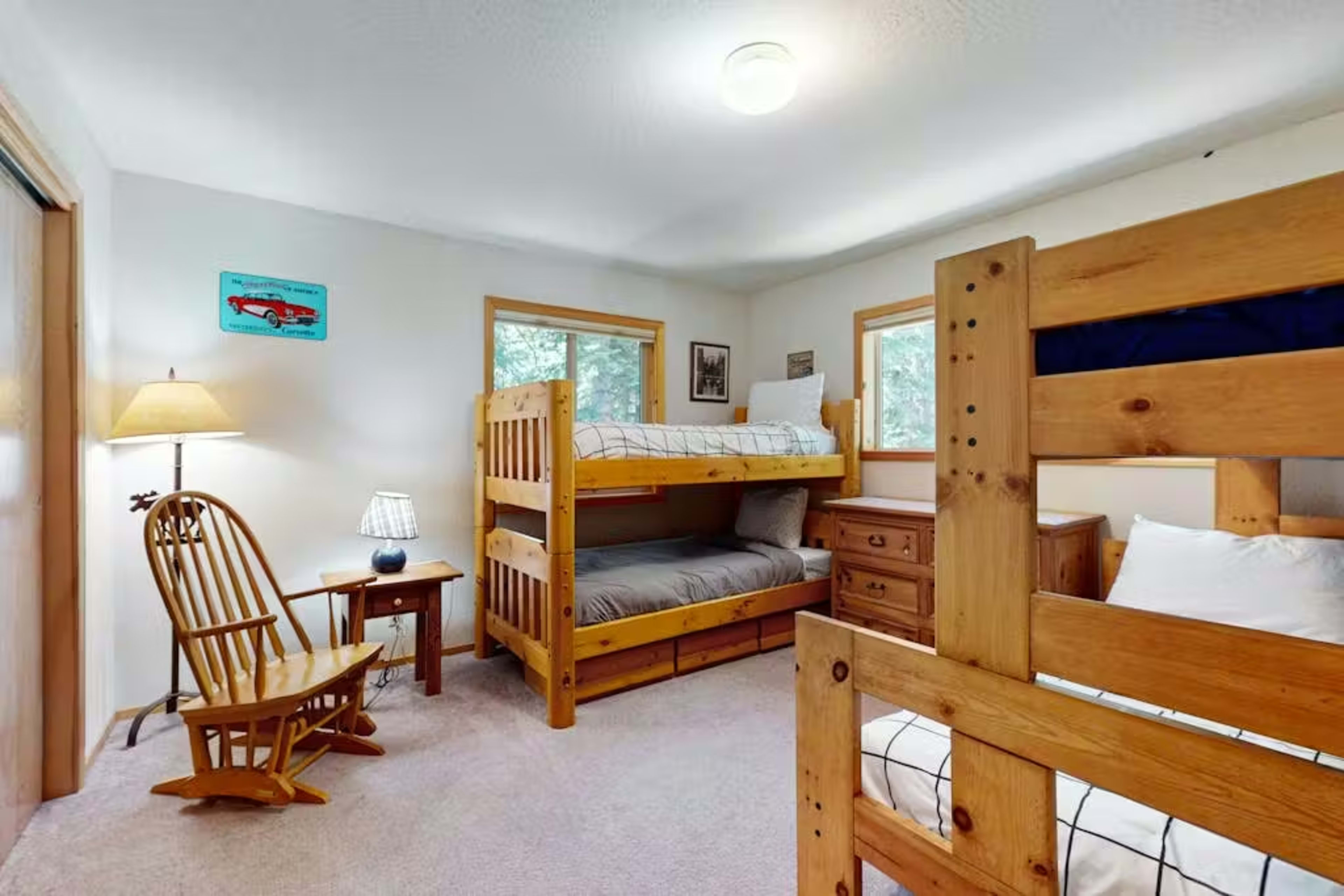 The image shows a cozy bedroom with a bunk bed, a rocking chair, and a bedside table next to a window.