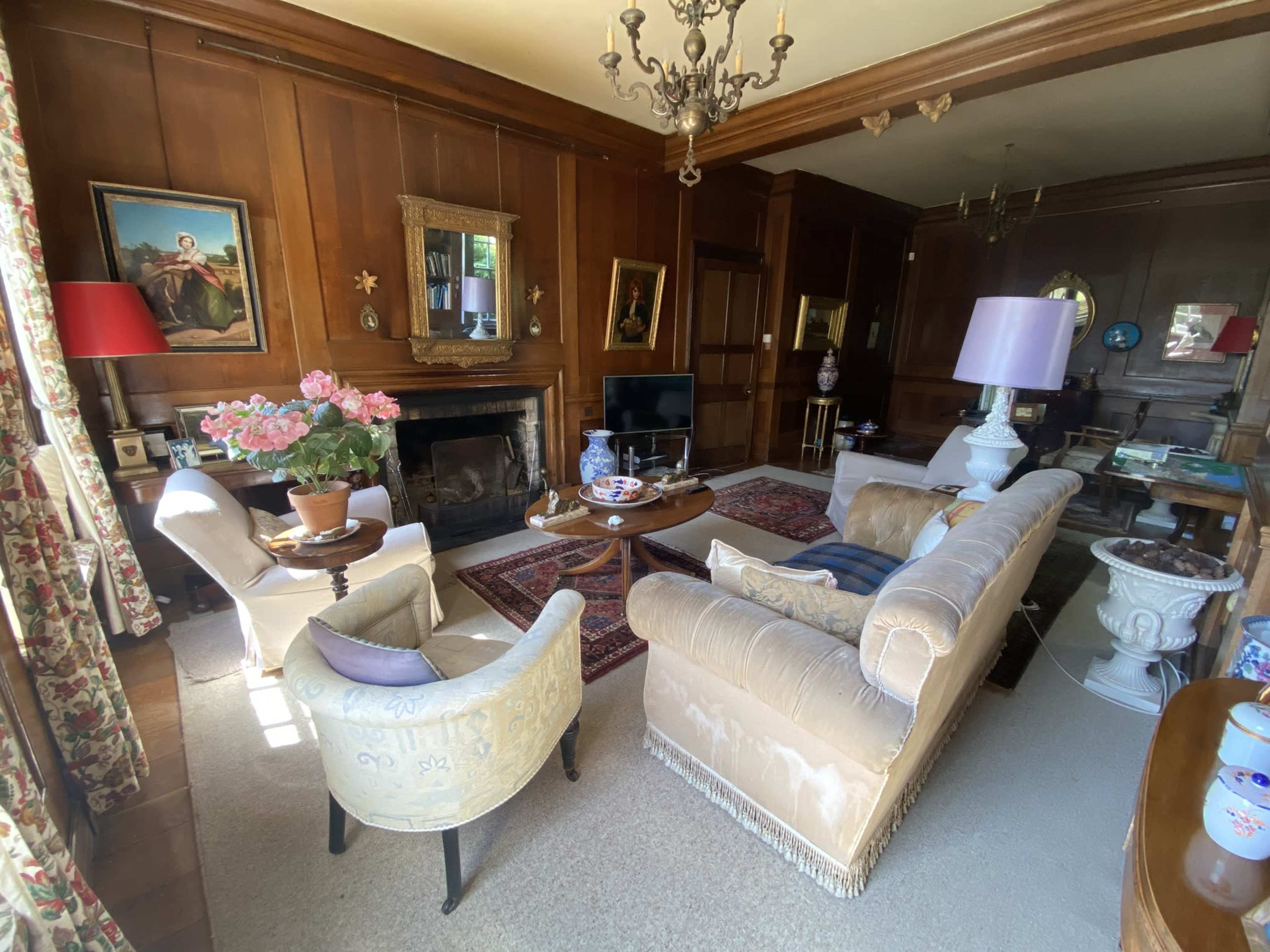 The image shows a cozy living room with wooden paneling, a fireplace, plush sofas, and various decorative elements.