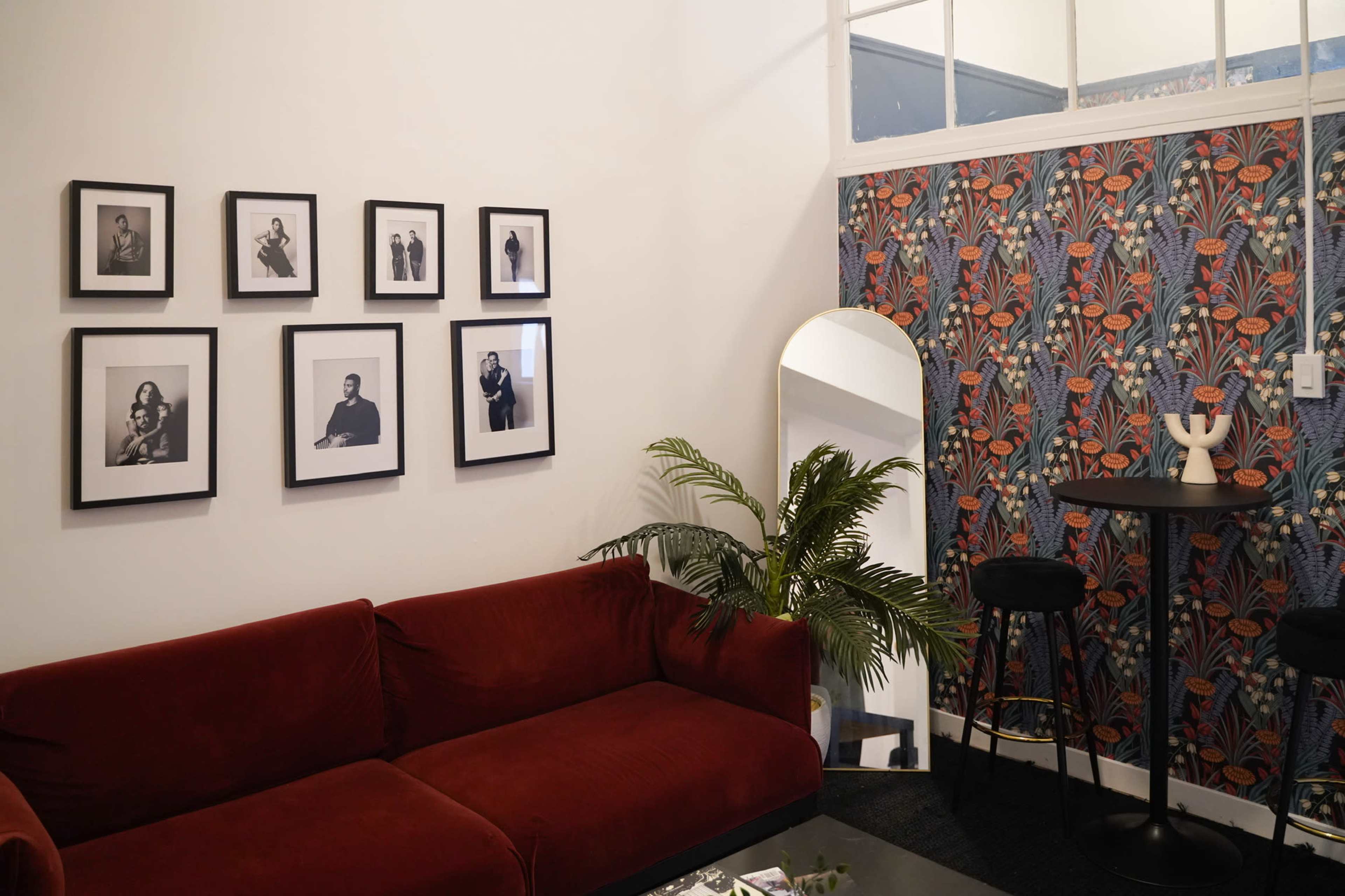 A living room with a red sofa, a patterned wallpaper on one side, and framed black-and-white photographs on the wall.