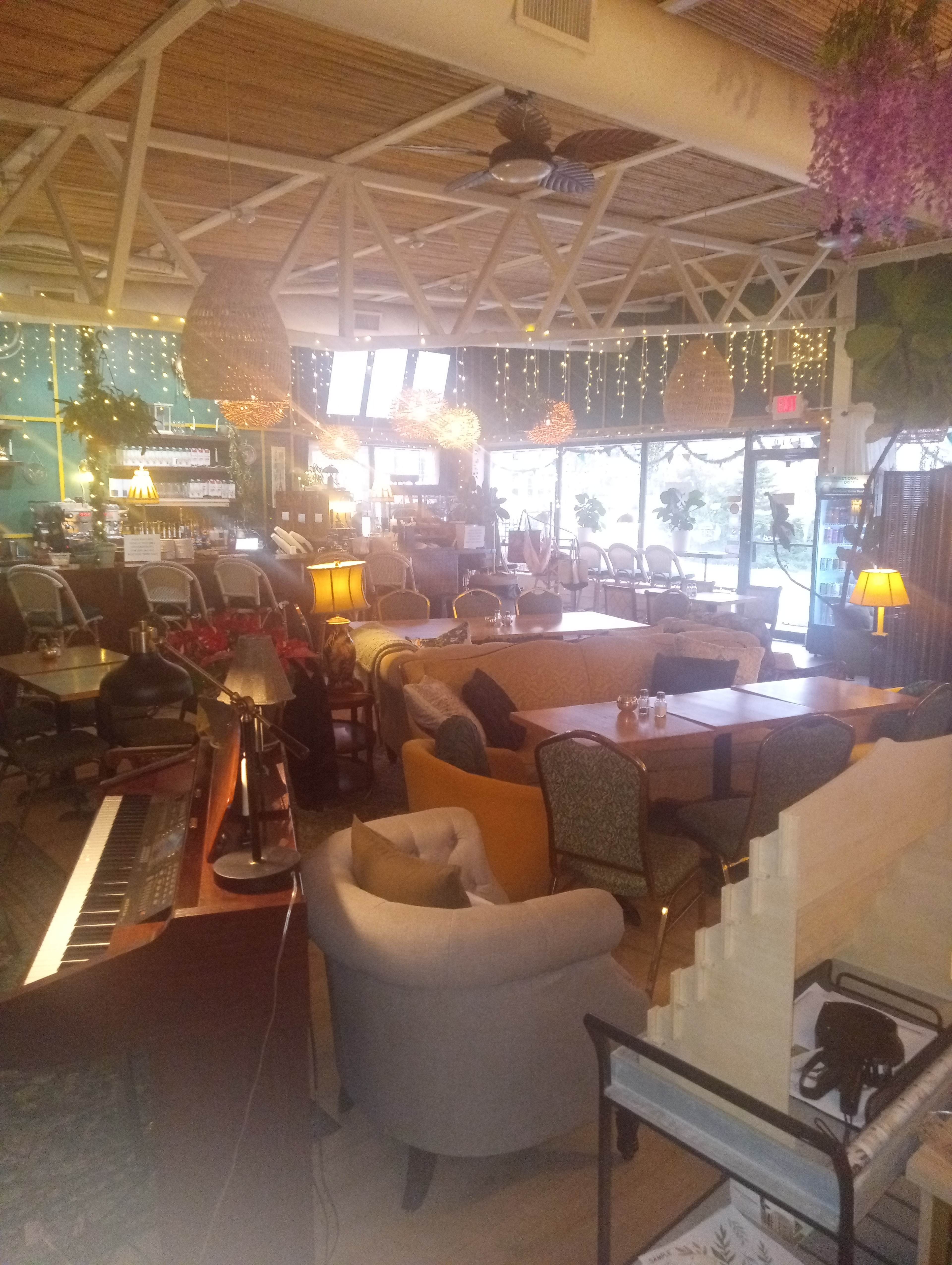 The image shows a café interior with various seating areas, including sofas and chairs, along with decorative lighting and a piano in one corner.