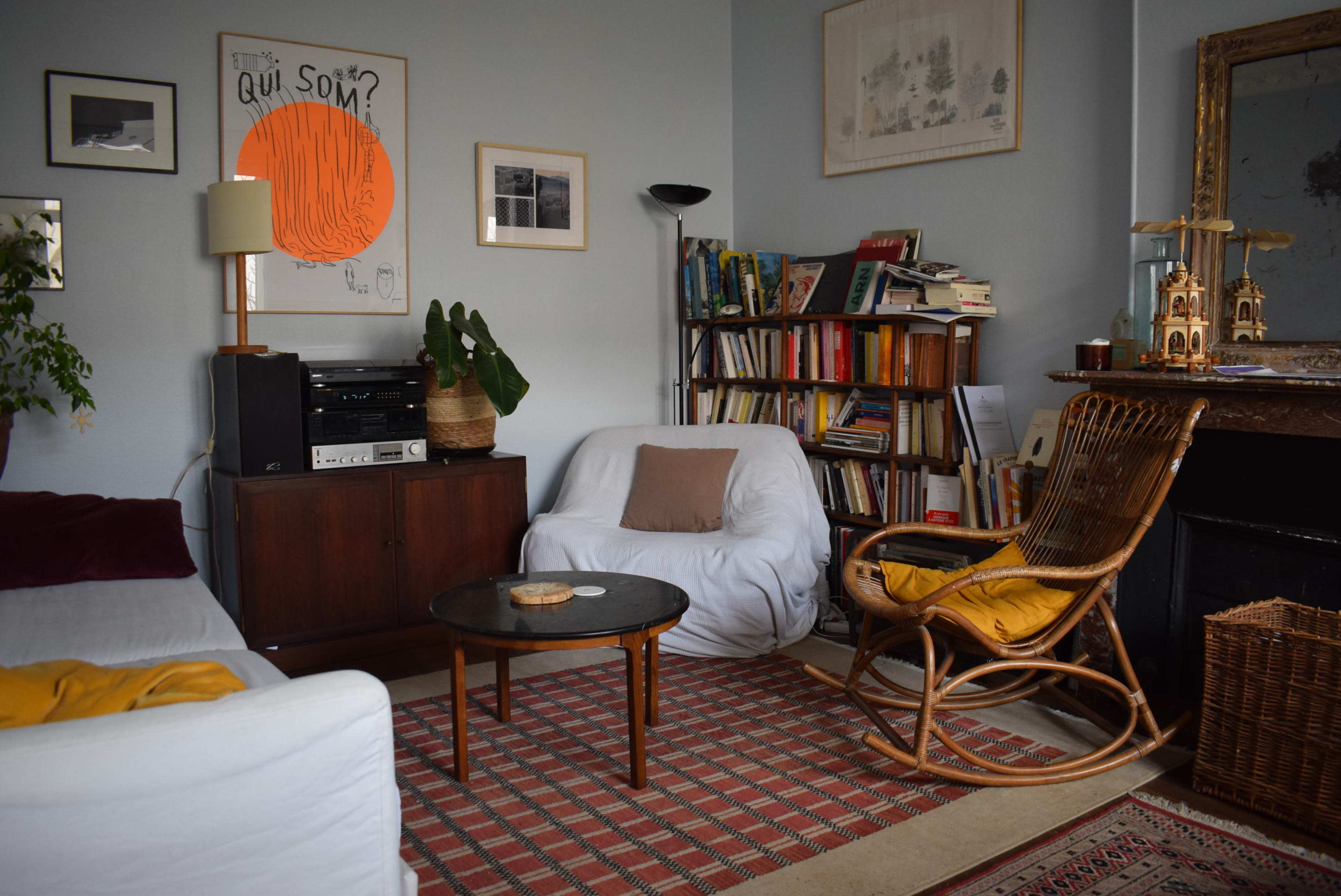 The image shows a cozy living room with a bookshelf, a vintage record player, two white chairs, and a circular coffee table on a patterned rug.