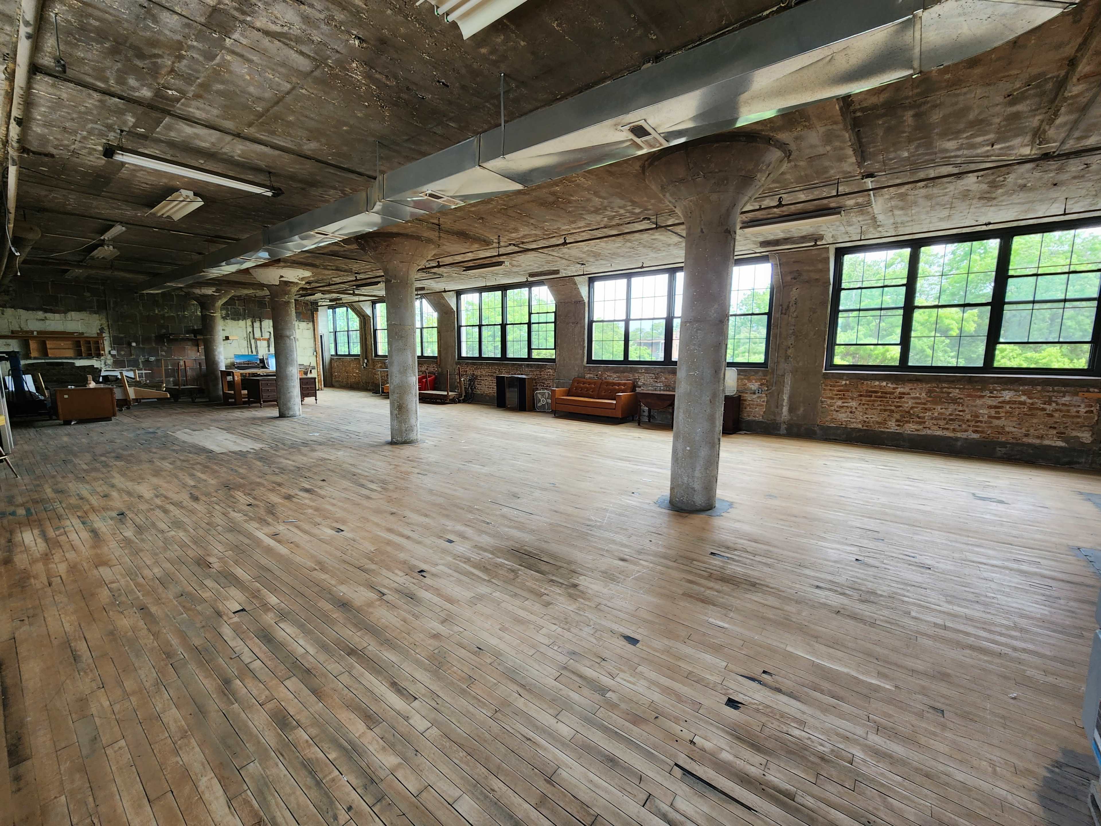 An empty industrial space with wooden floors, large windows, and concrete pillars.