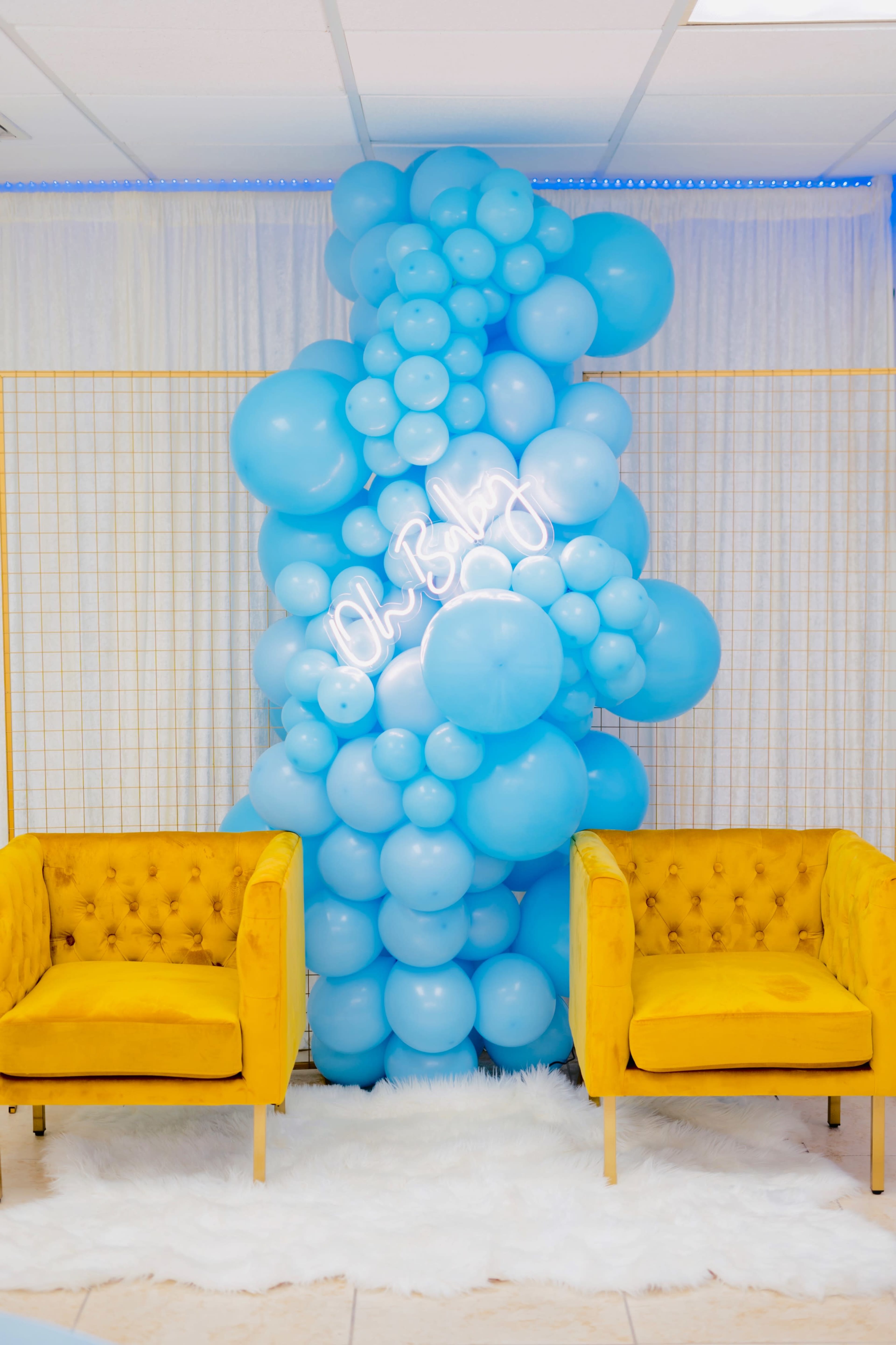 A display features a cluster of blue balloons next to two yellow tufted chairs on a white rug.