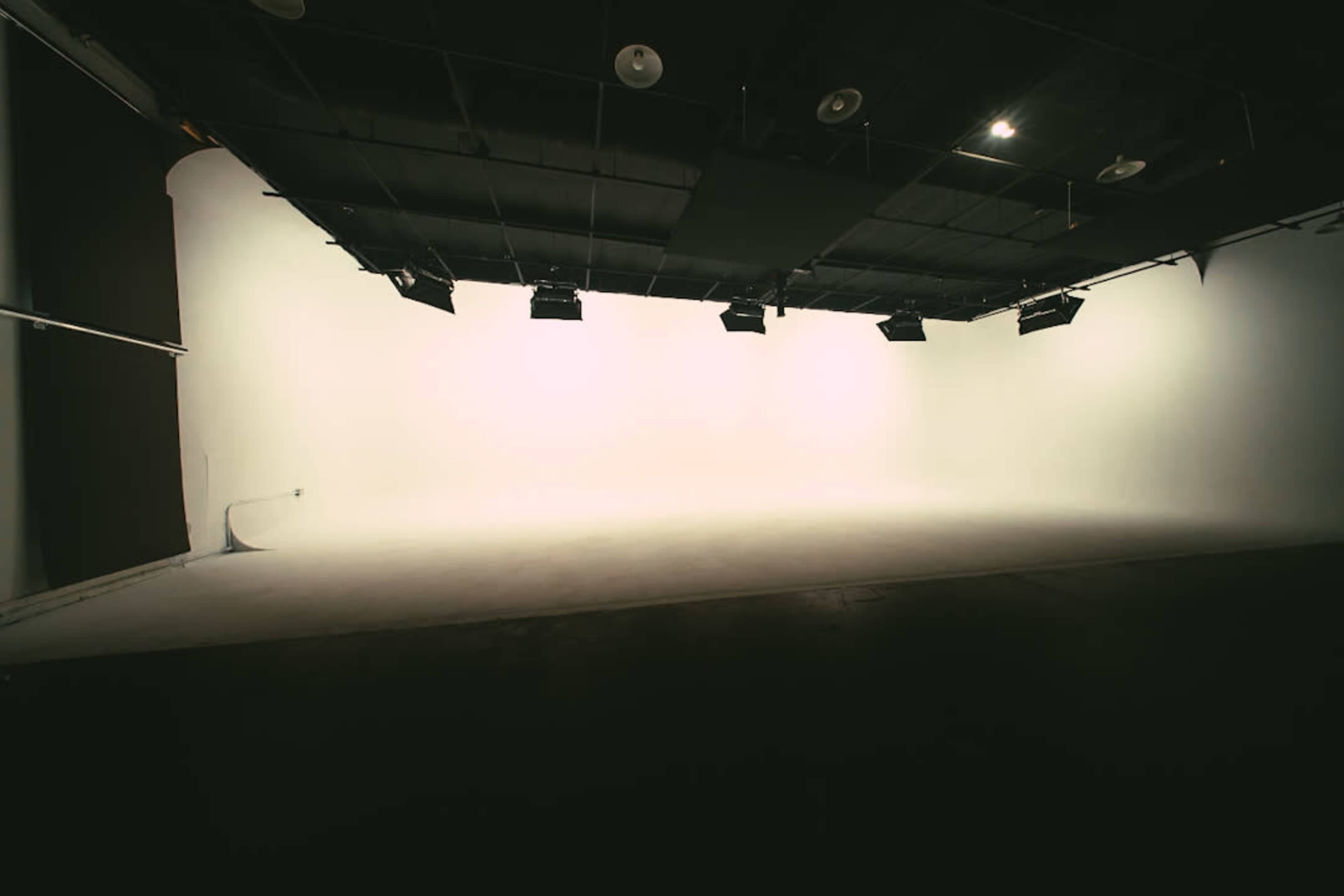 The image shows a large, empty studio space with a smooth white backdrop and overhead lighting.