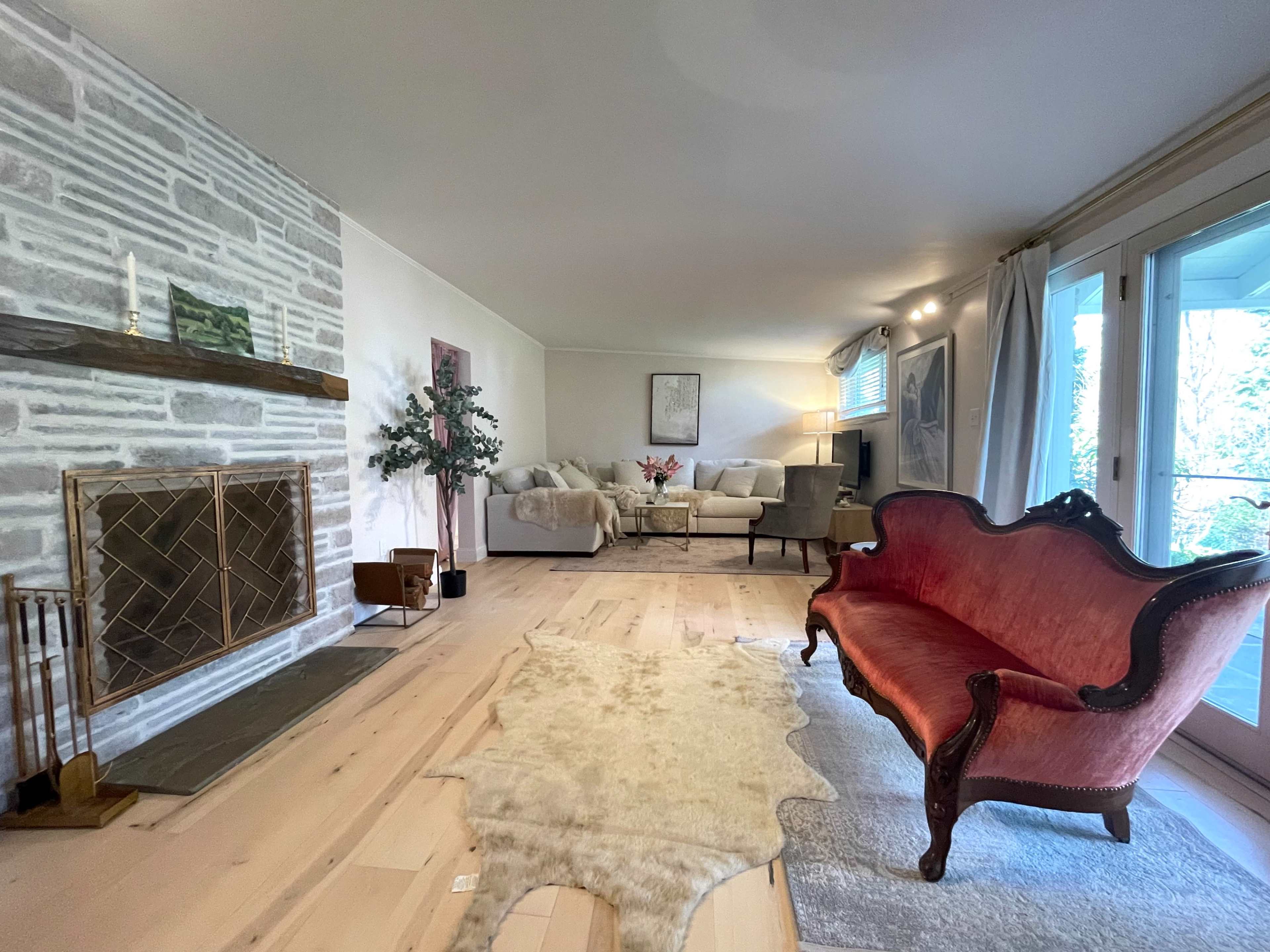 A spacious living room featuring a stone fireplace, a red upholstered loveseat, and a seating area with two light-colored couches and a coffee table.