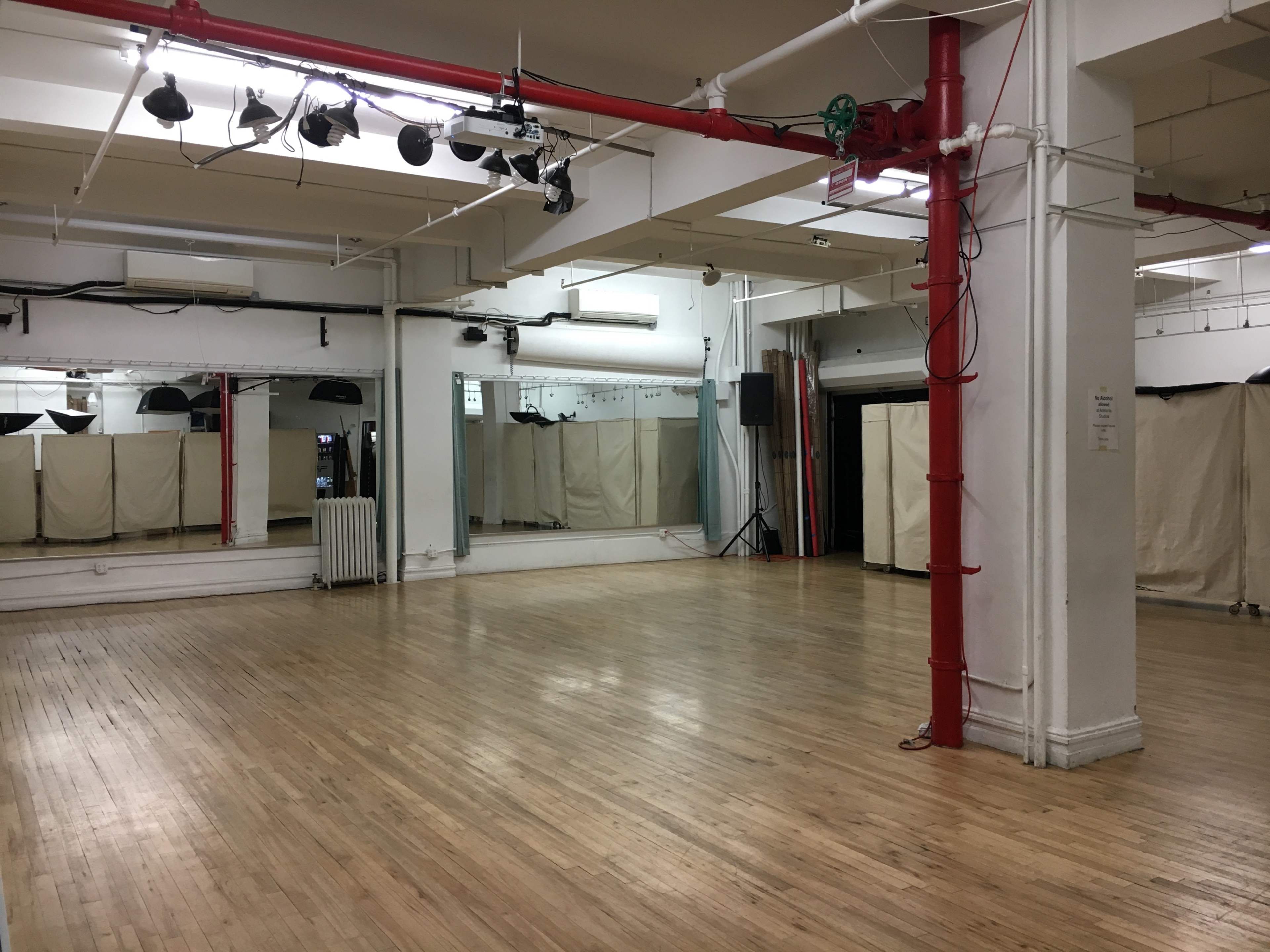 The image shows an empty dance studio with a polished wooden floor, mirrored walls, and red support beams.