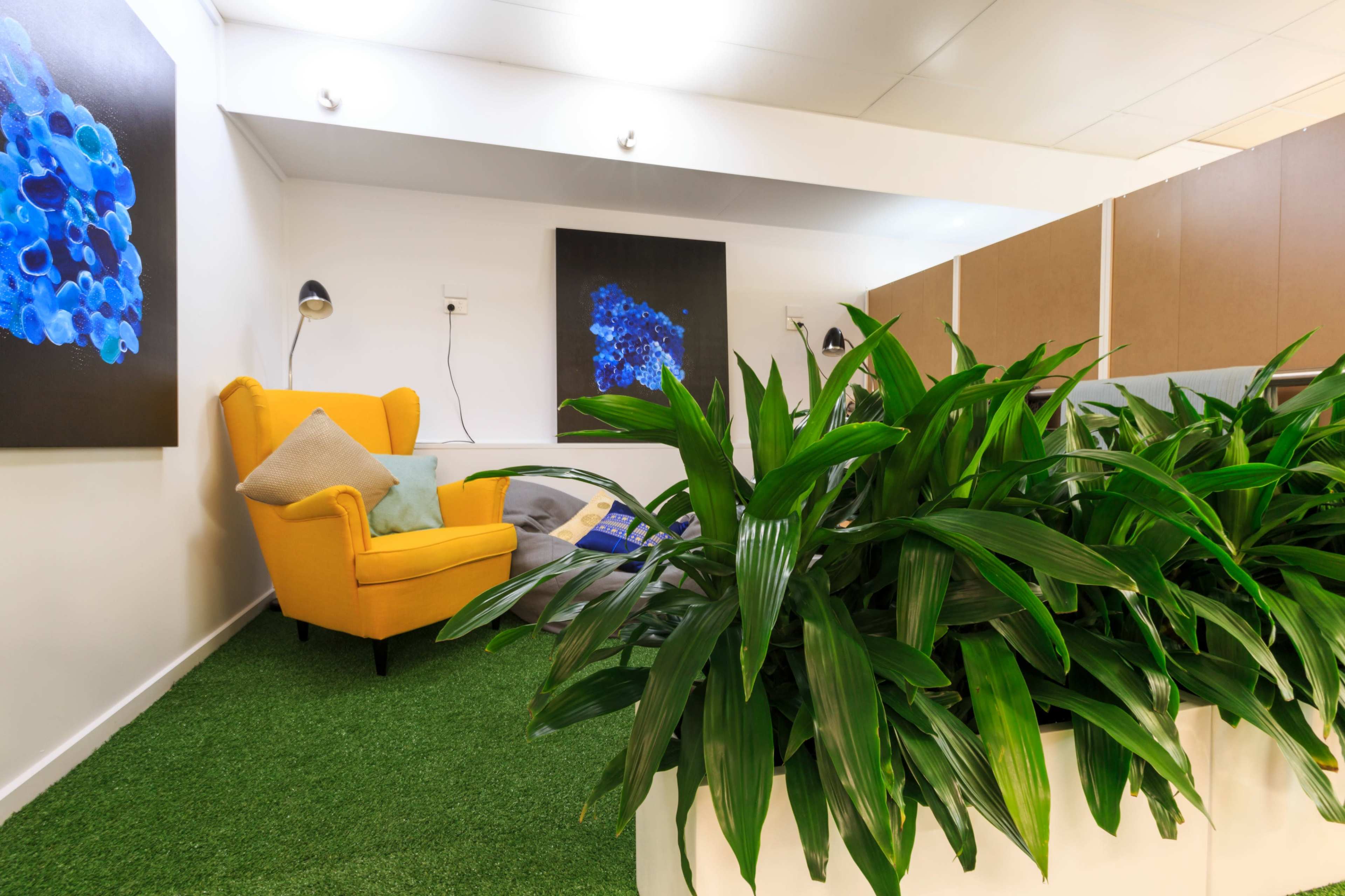 The image shows a cozy seating area with a yellow armchair, decorative plants, and modern artwork on the walls.