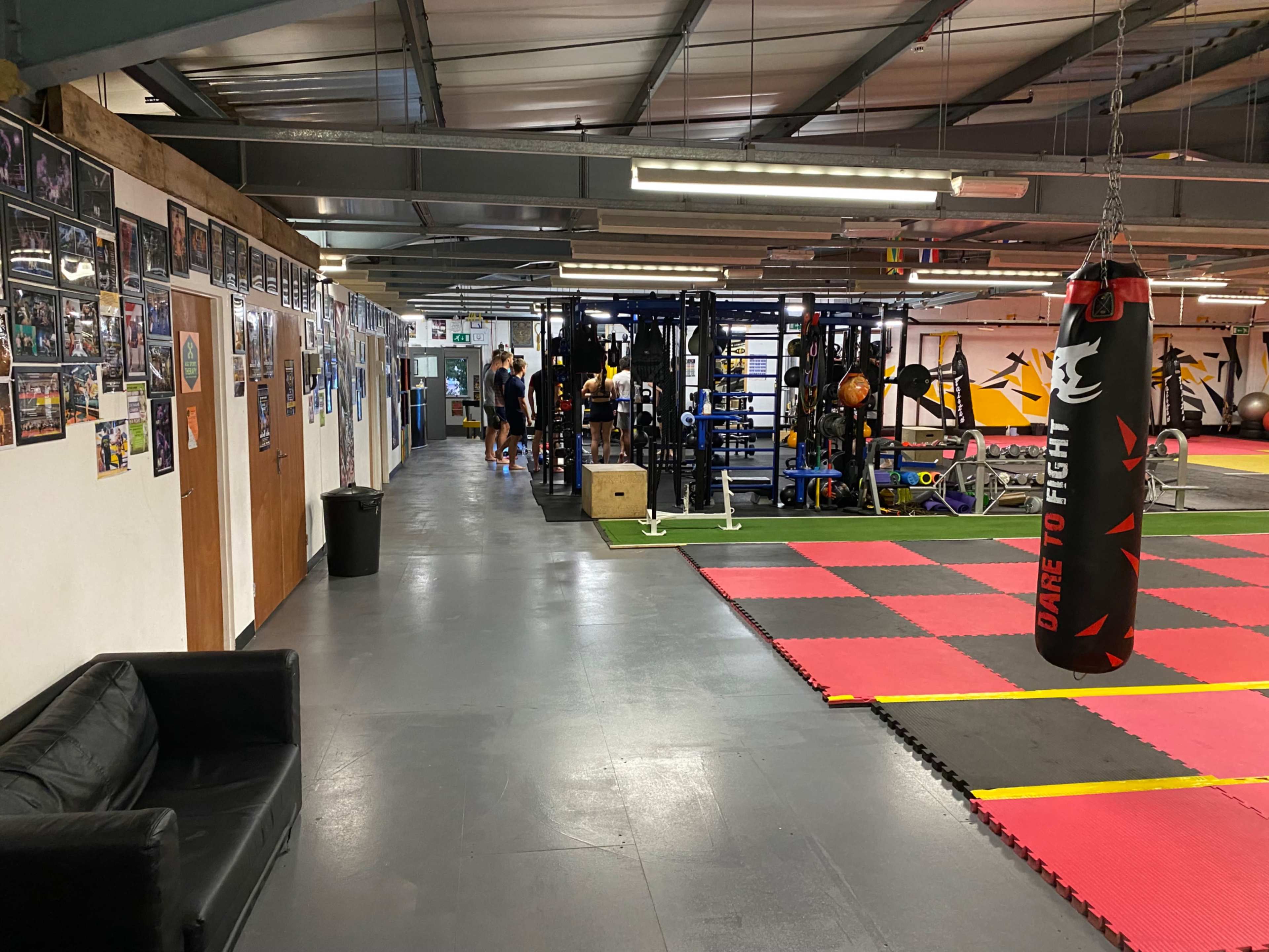 The image shows a gym interior featuring workout equipment, a boxing bag, and a wall adorned with framed photos.