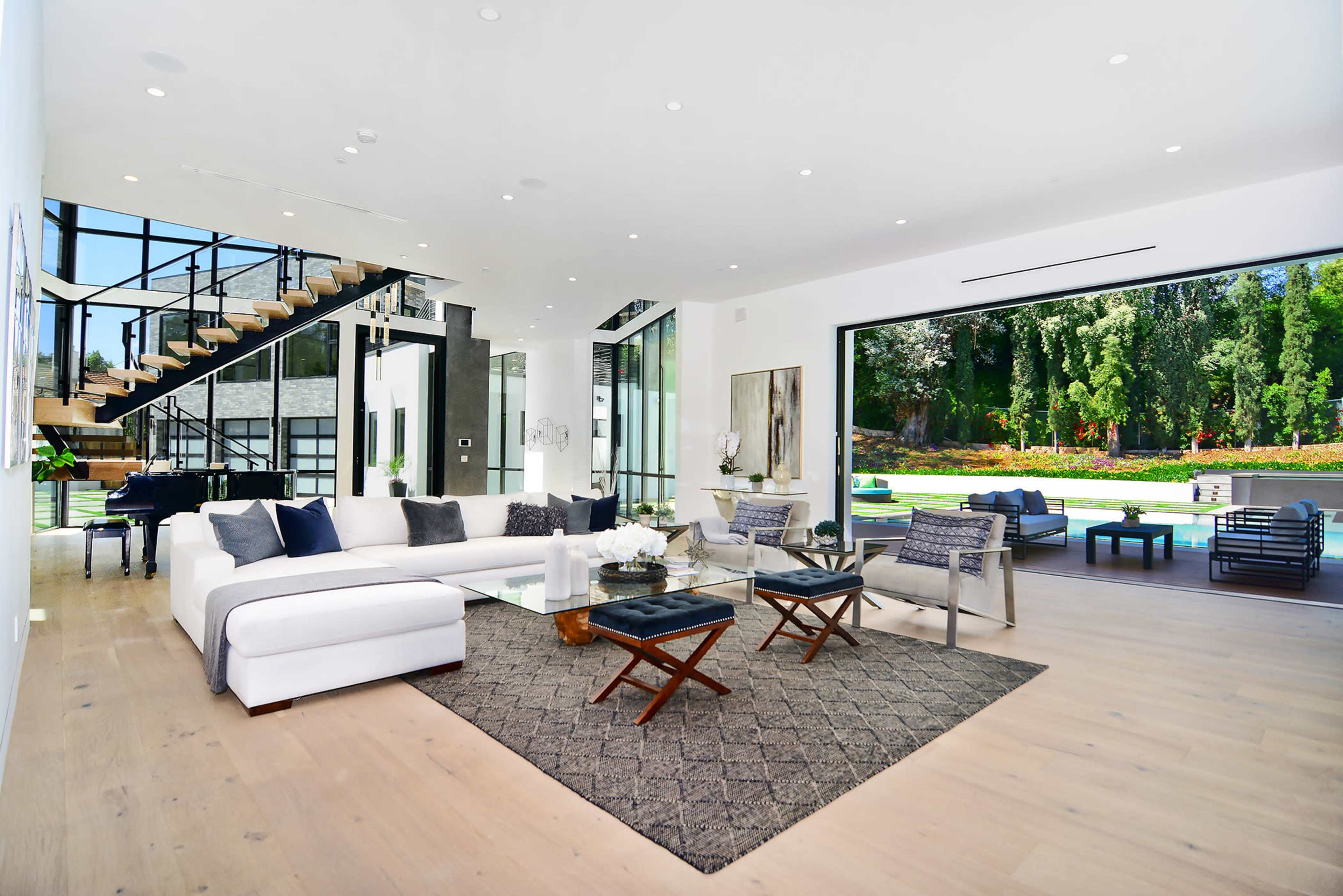A modern living room features a large white sectional sofa, a glass coffee table, and a view of a pool area through expansive sliding doors.