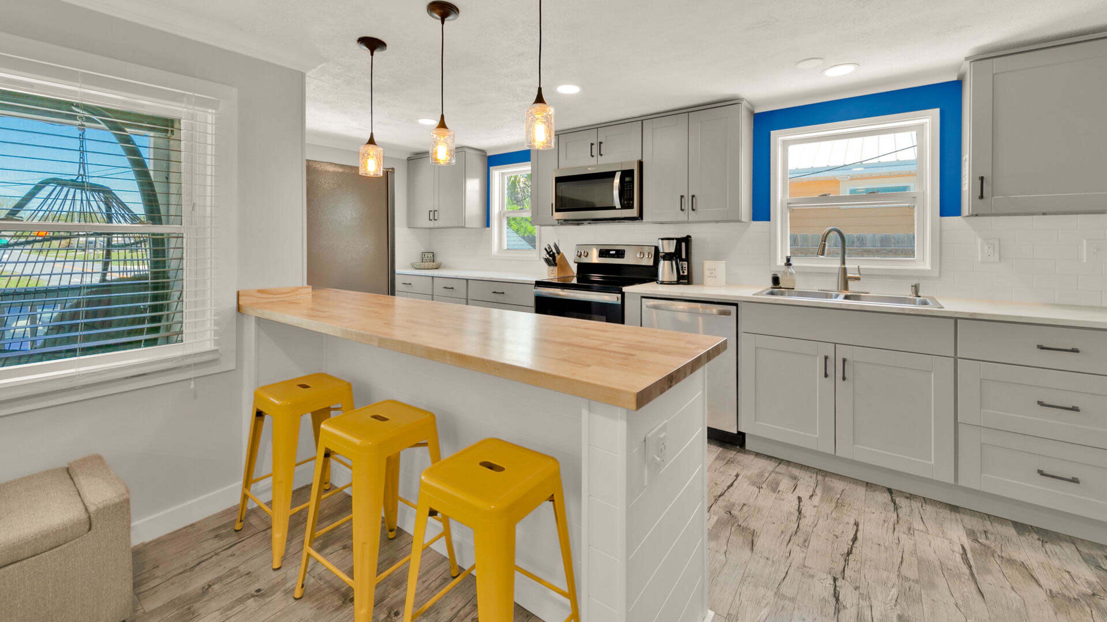 A modern kitchen features gray cabinets, stainless steel appliances, and a wooden countertop with three yellow bar stools.