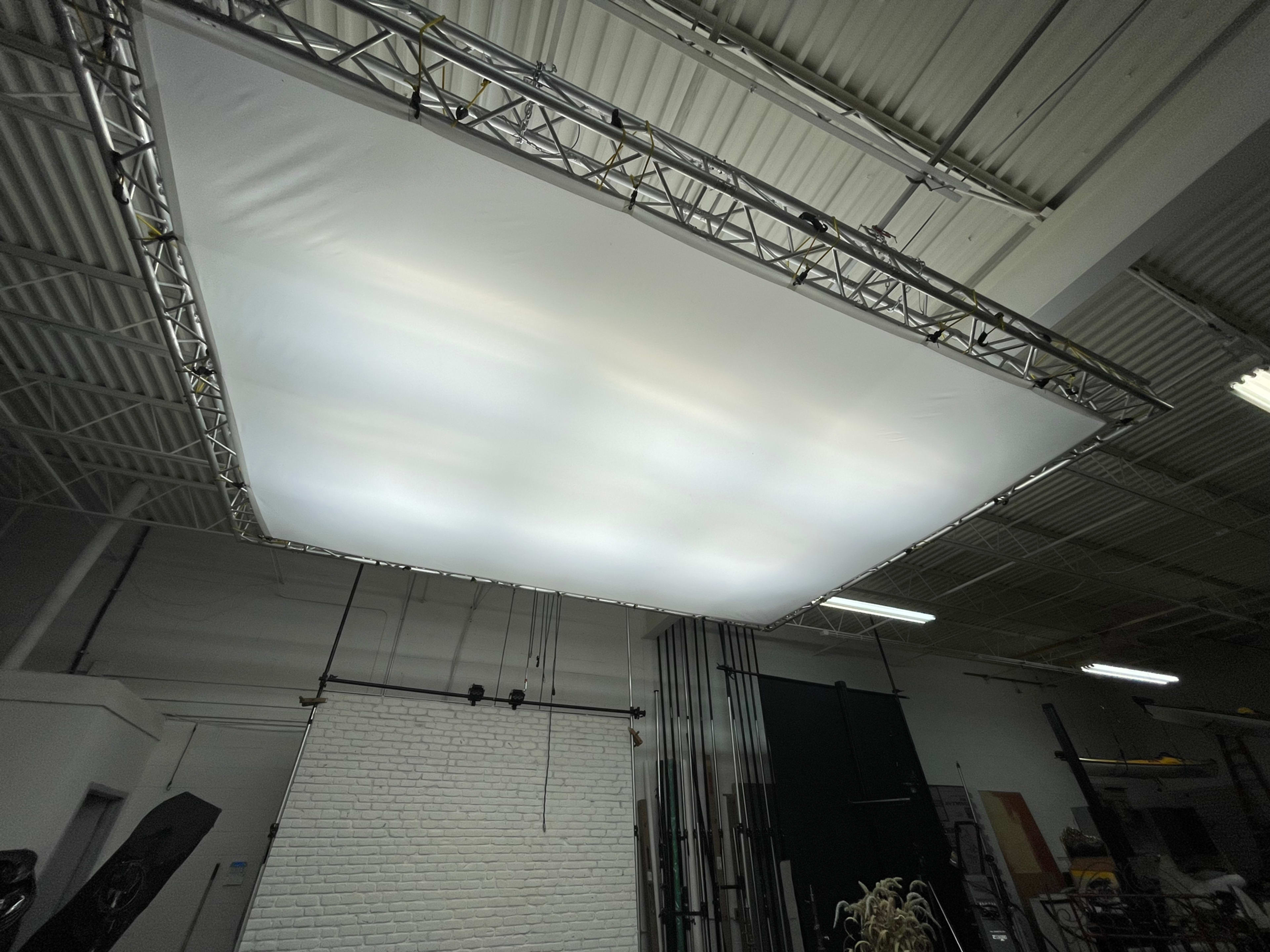 A large, white diffusion panel is suspended from a metal frame in a studio space.