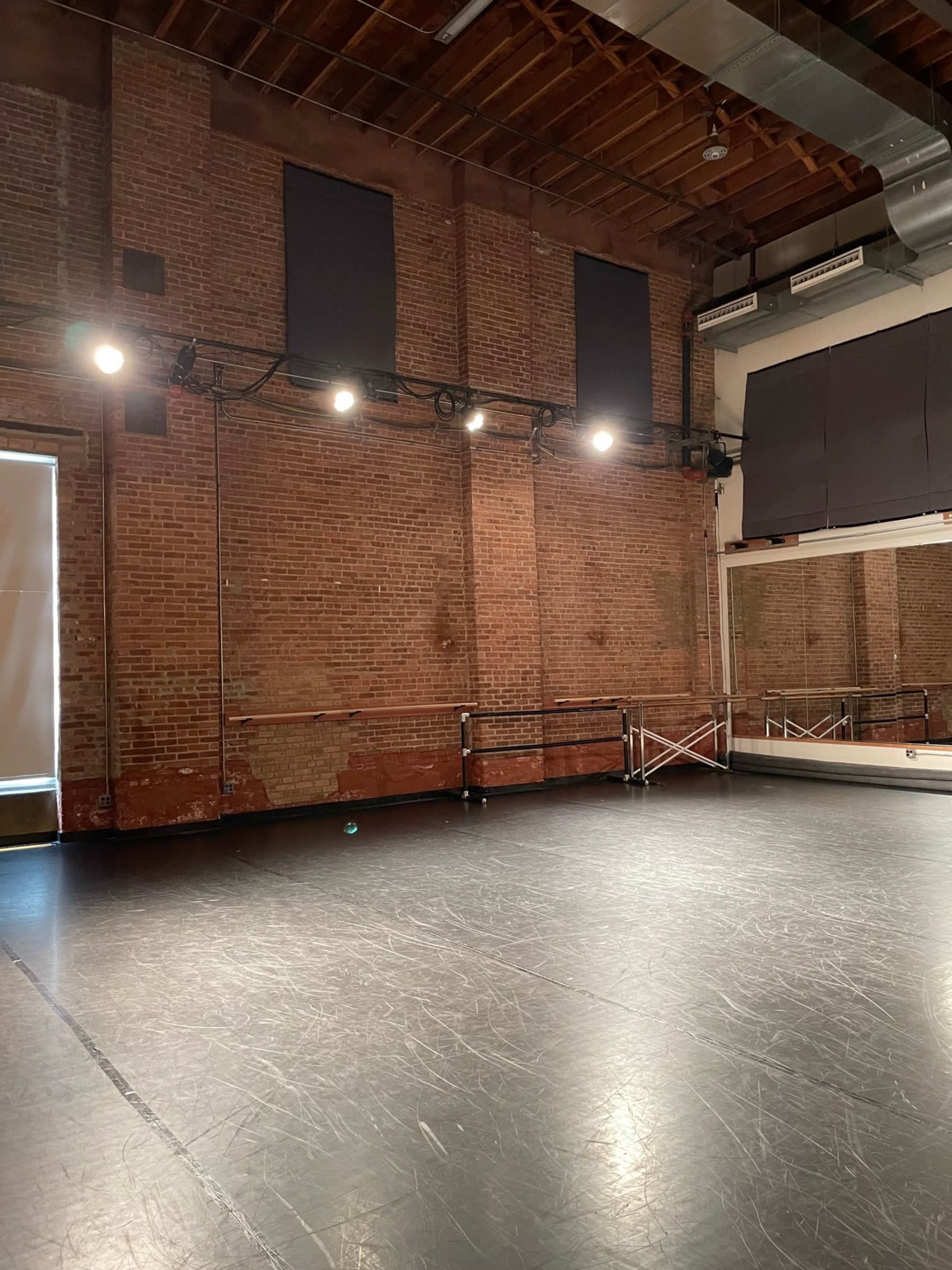 A wooden-floored dance studio with brick walls and stage lighting installed along the ceiling.