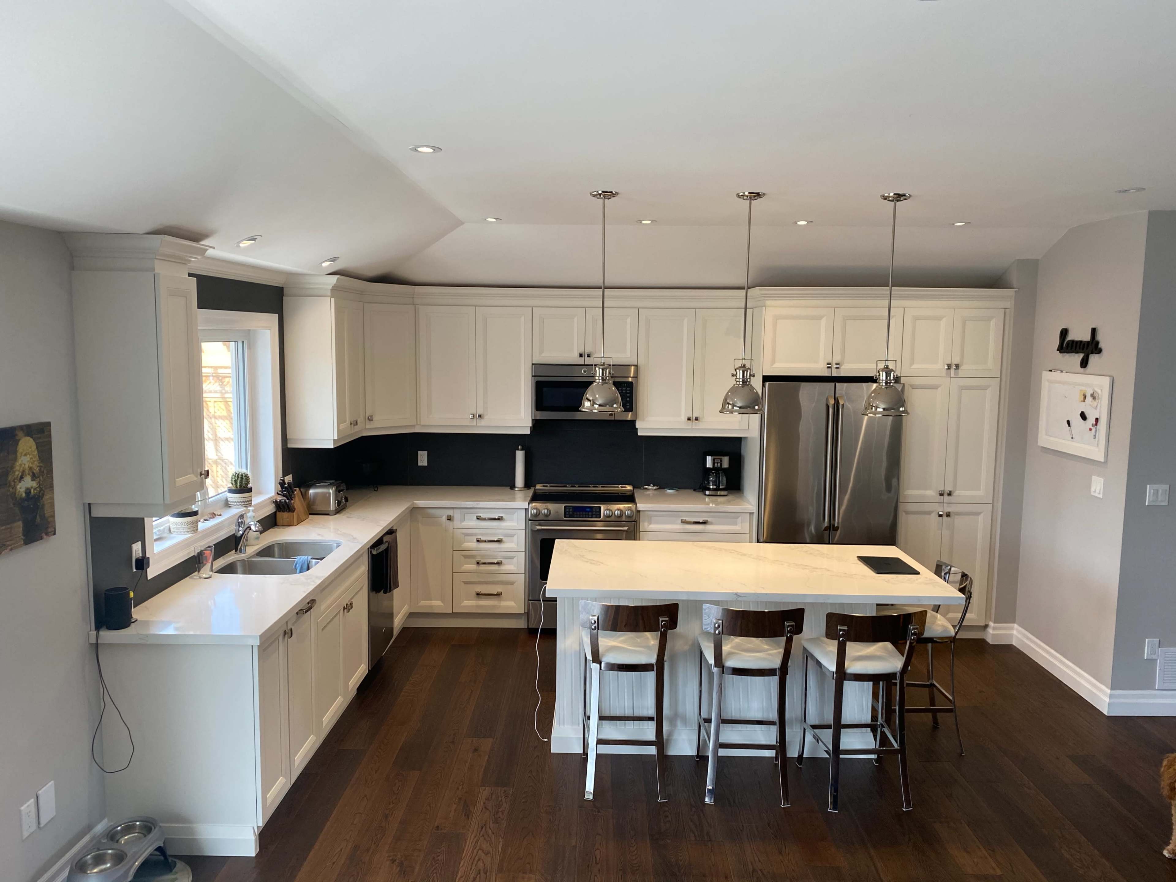 The modern kitchen features white cabinetry, a central island with seating, stainless steel appliances, and hardwood flooring.