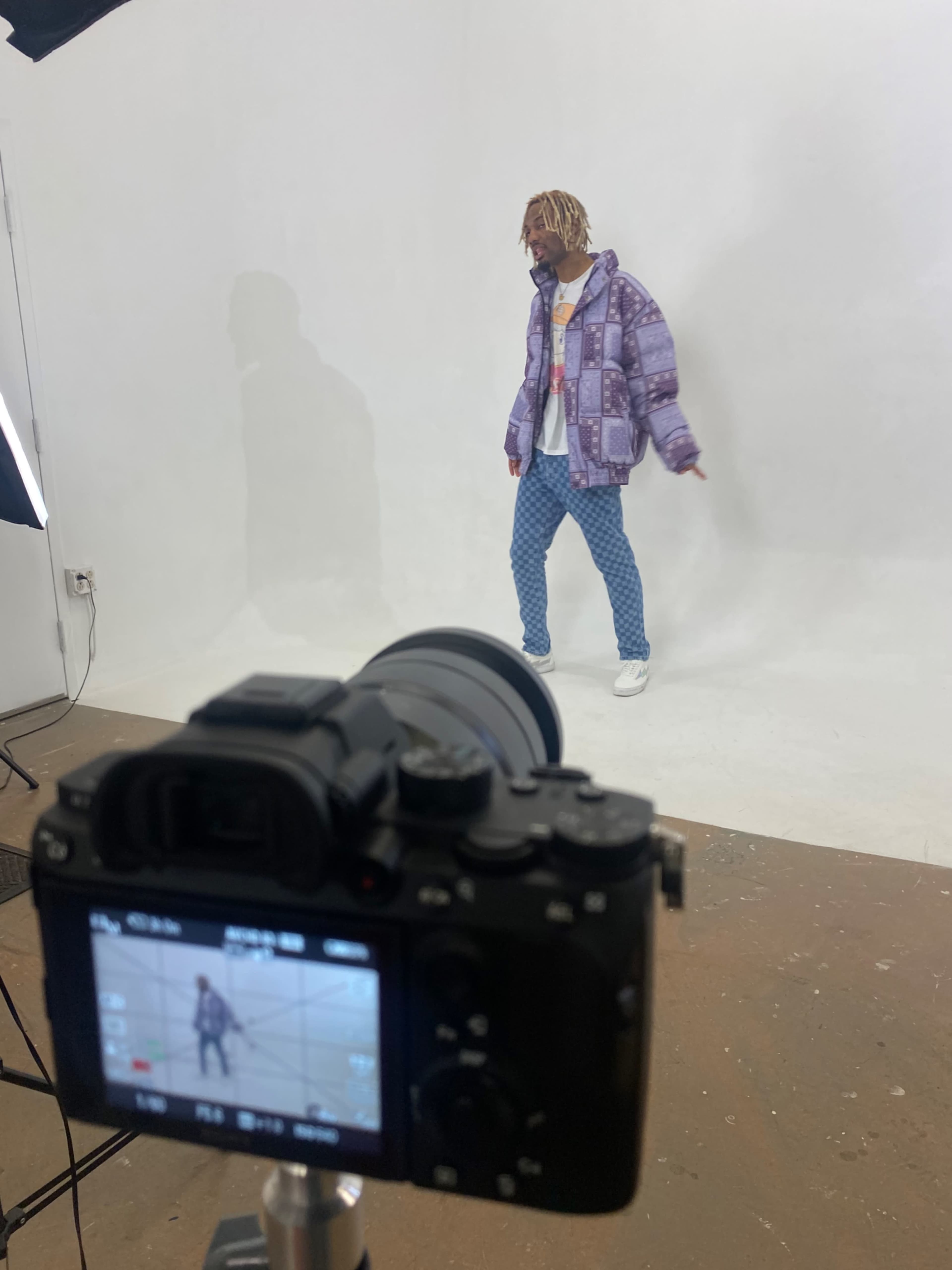 A photographer captures a model wearing a patterned jacket and denim jeans in a studio setting.