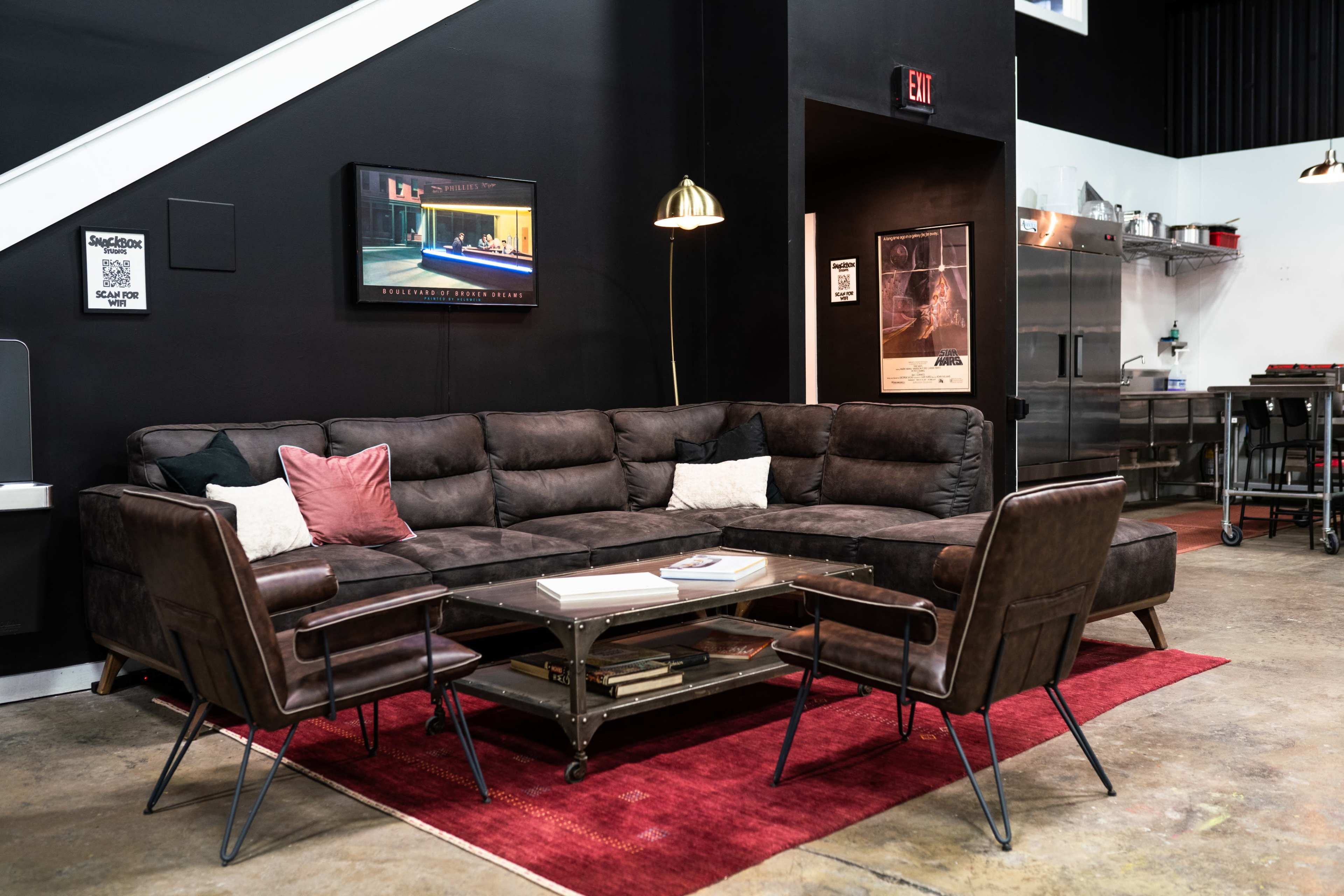 A modern living room featuring a dark sectional sofa, two armchairs, a glass coffee table, and a television mounted on the wall.