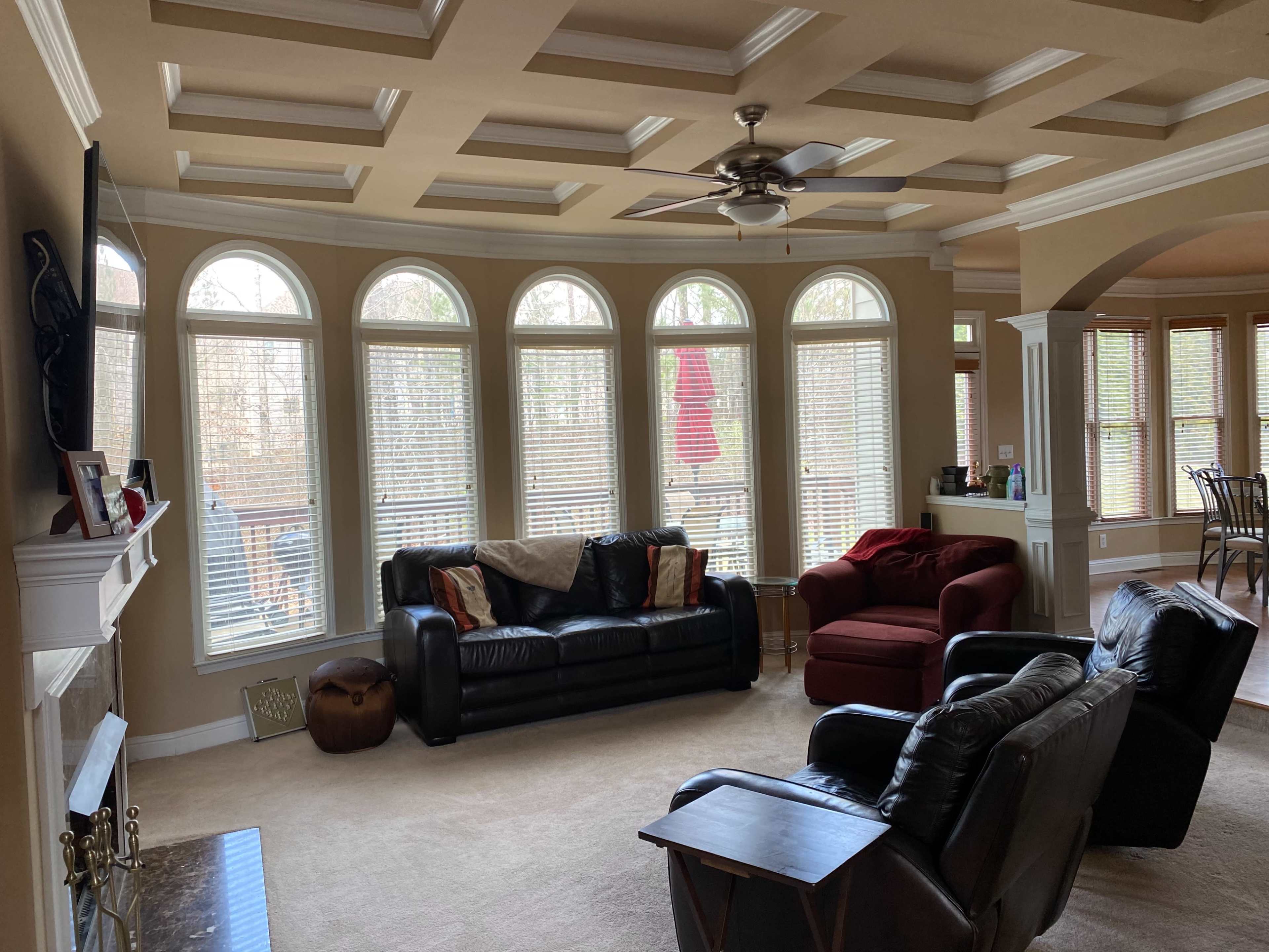 A spacious living room with a coffered ceiling, large arched windows, and a mix of black leather and red upholstered furniture.