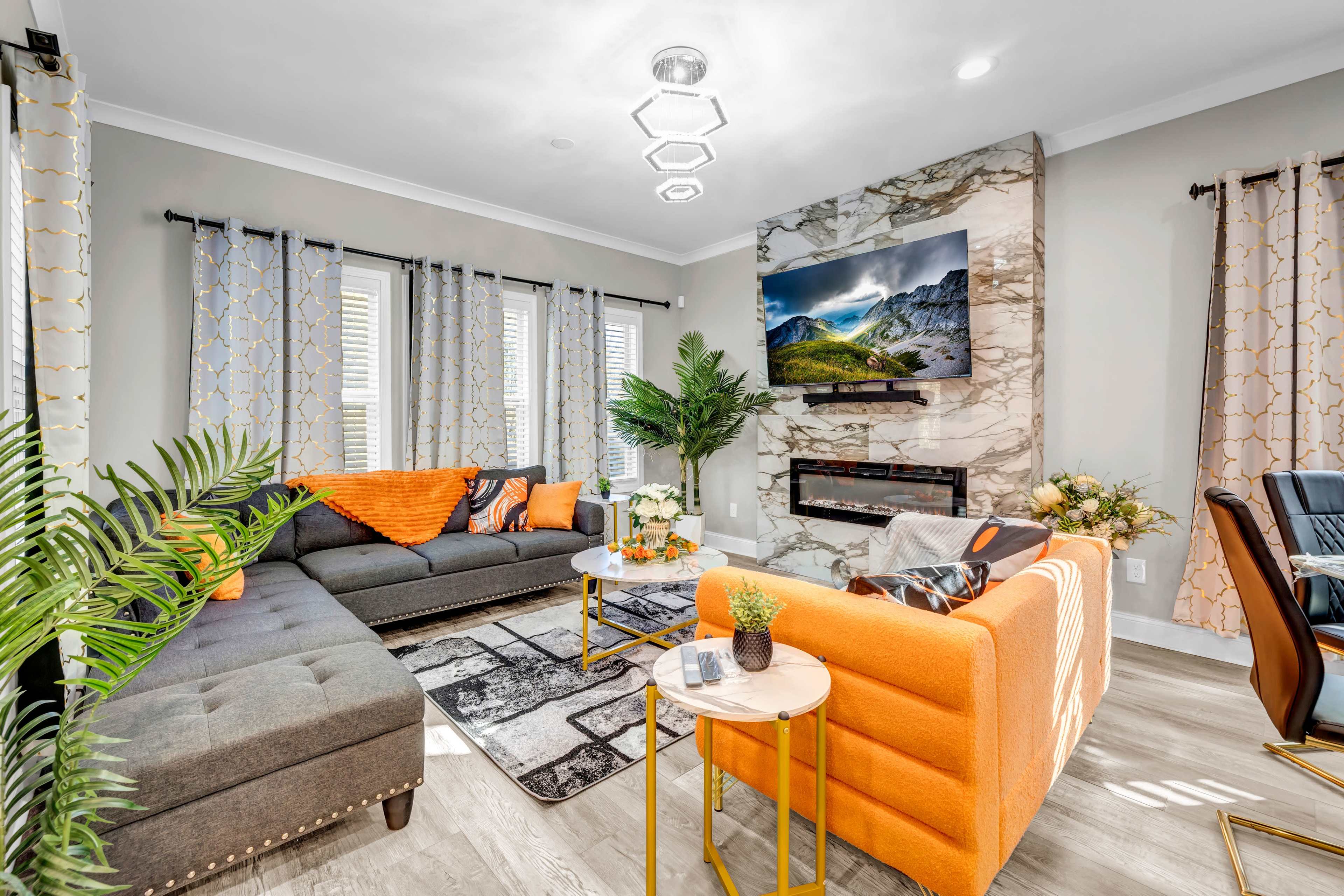 The living room features a dark sectional sofa and an orange accent chair, with a decorative table and large framed artwork above a modern fireplace.