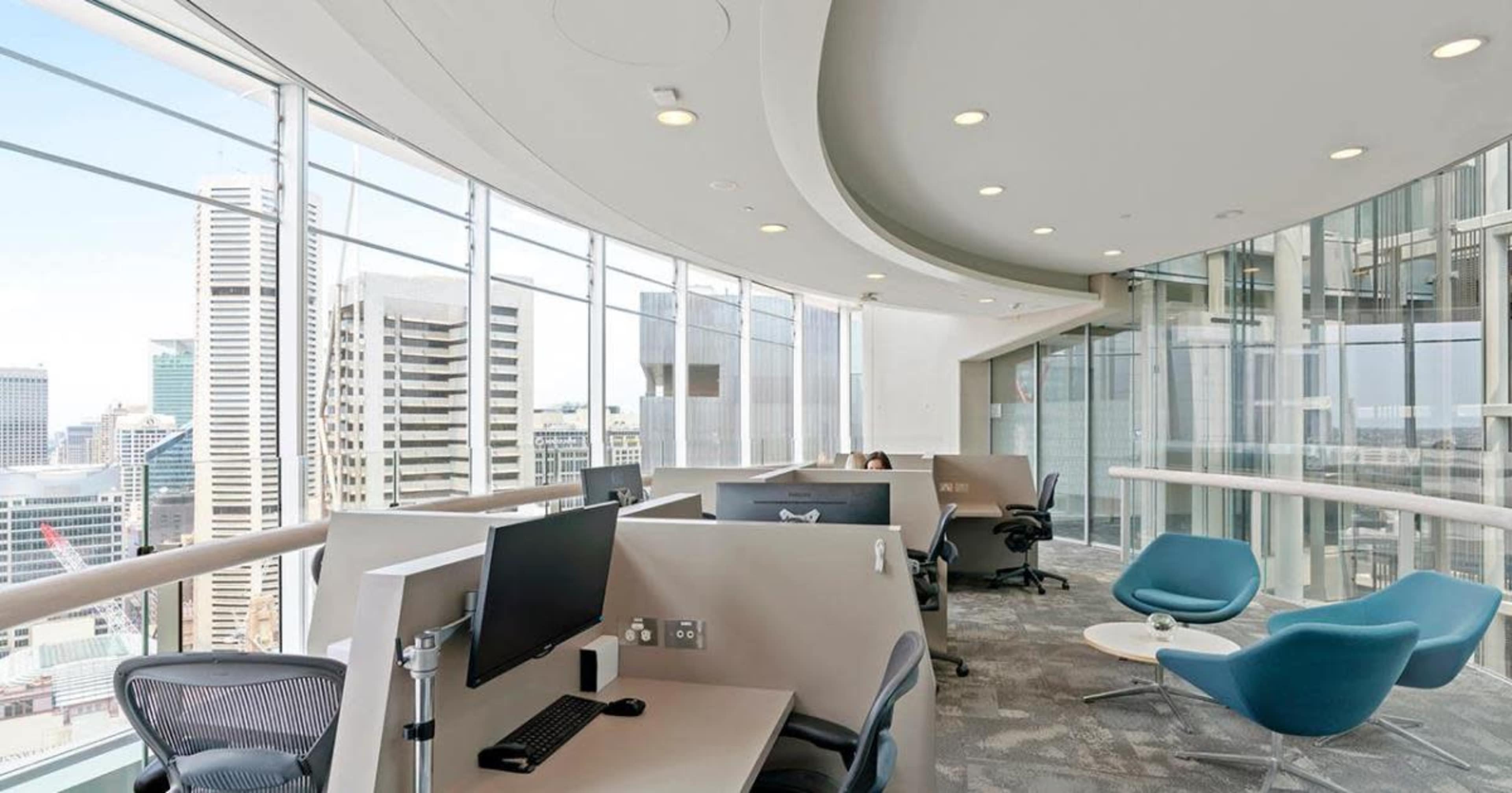 A modern office space with large windows, workstations equipped with computers, and contemporary chairs.