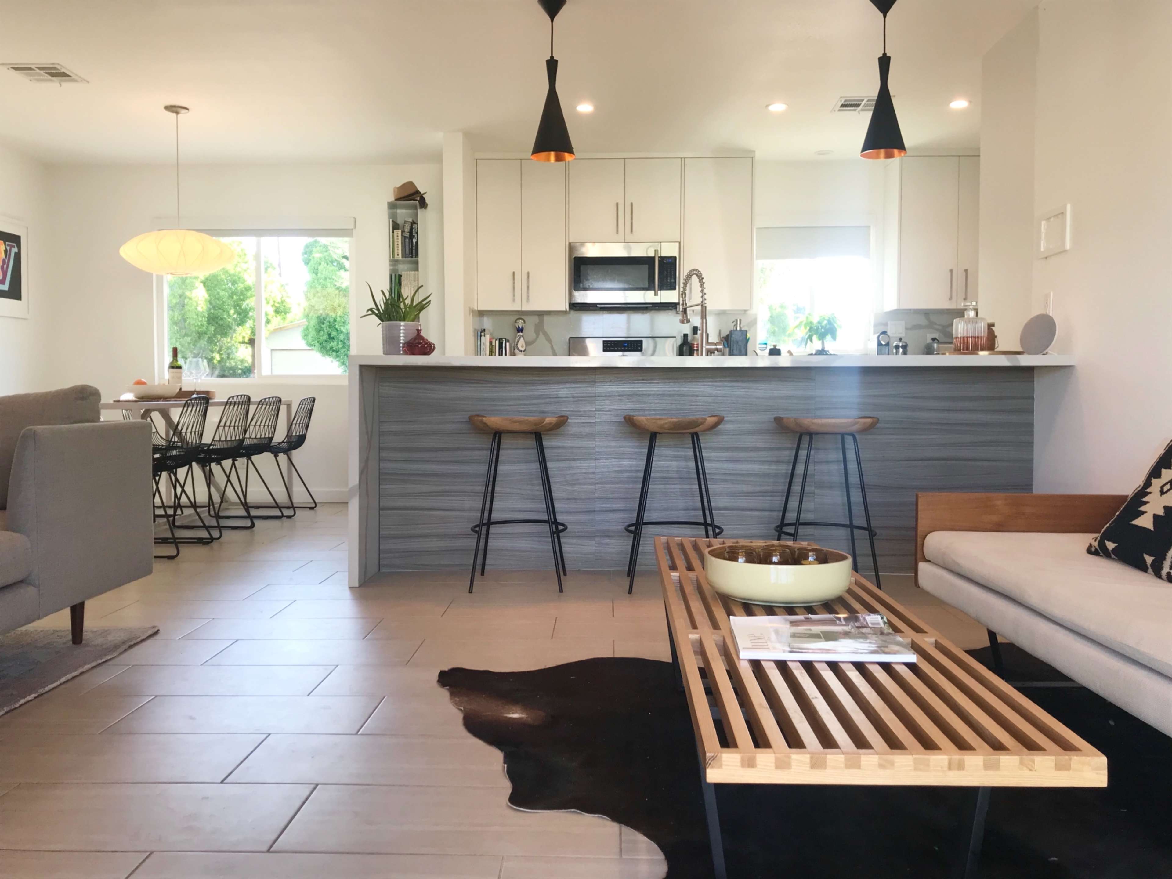 The image shows a modern open-concept living space featuring a kitchen with bar stools, a dining area with a table, and a seating area with a couch and coffee table.