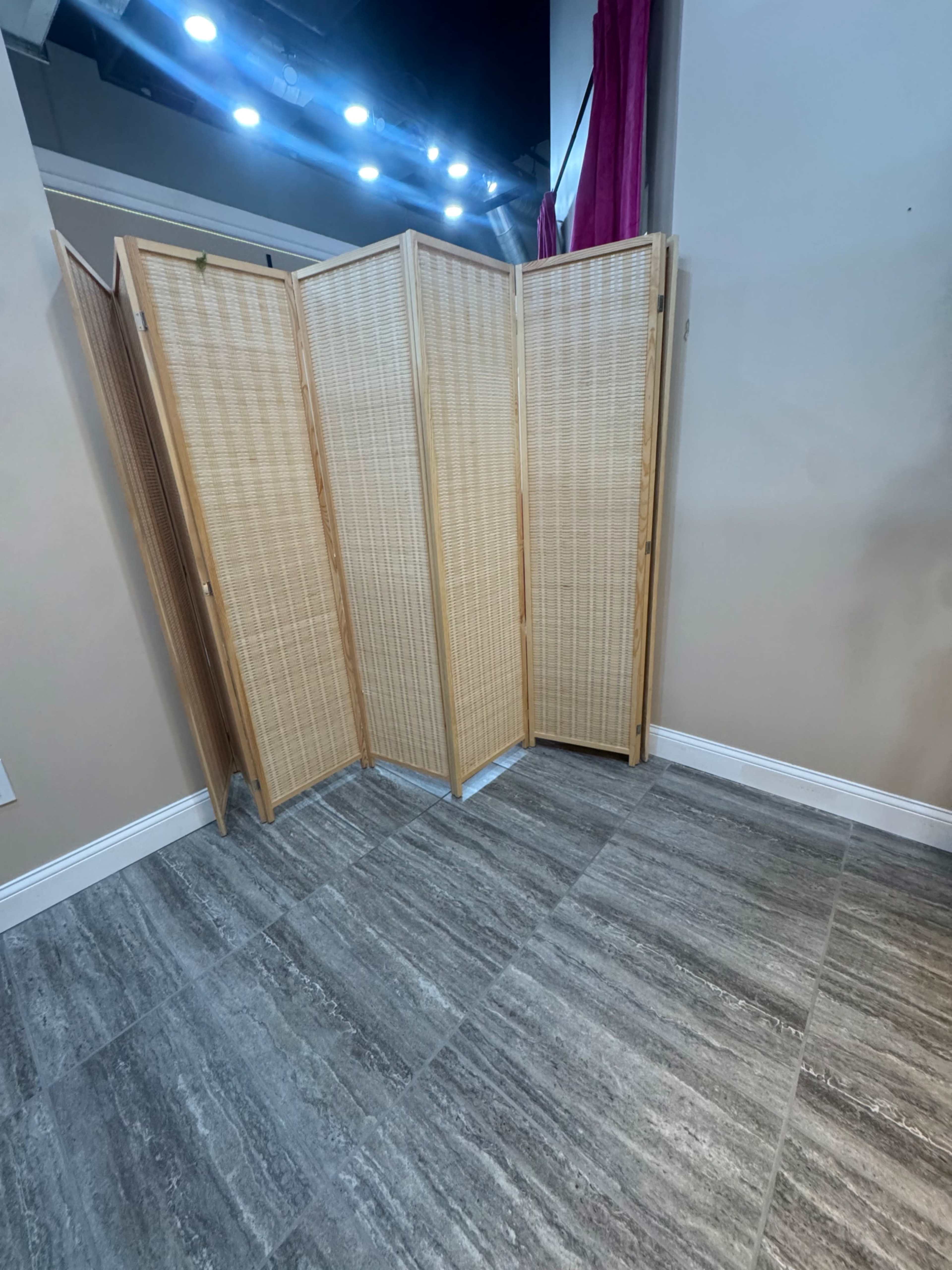 The image shows a wooden folding screen positioned in a corner of a room with gray tiled flooring.