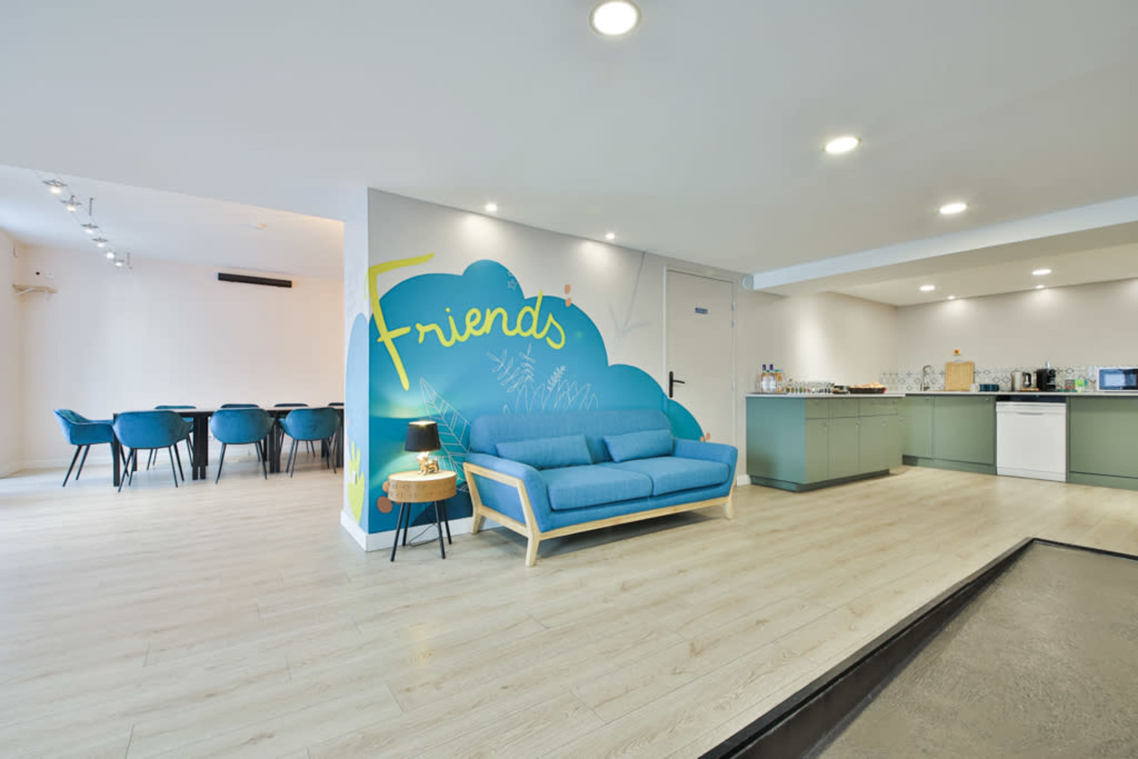 A modern living space featuring a blue couch, a kitchen area with appliances, and a dining table in the background.