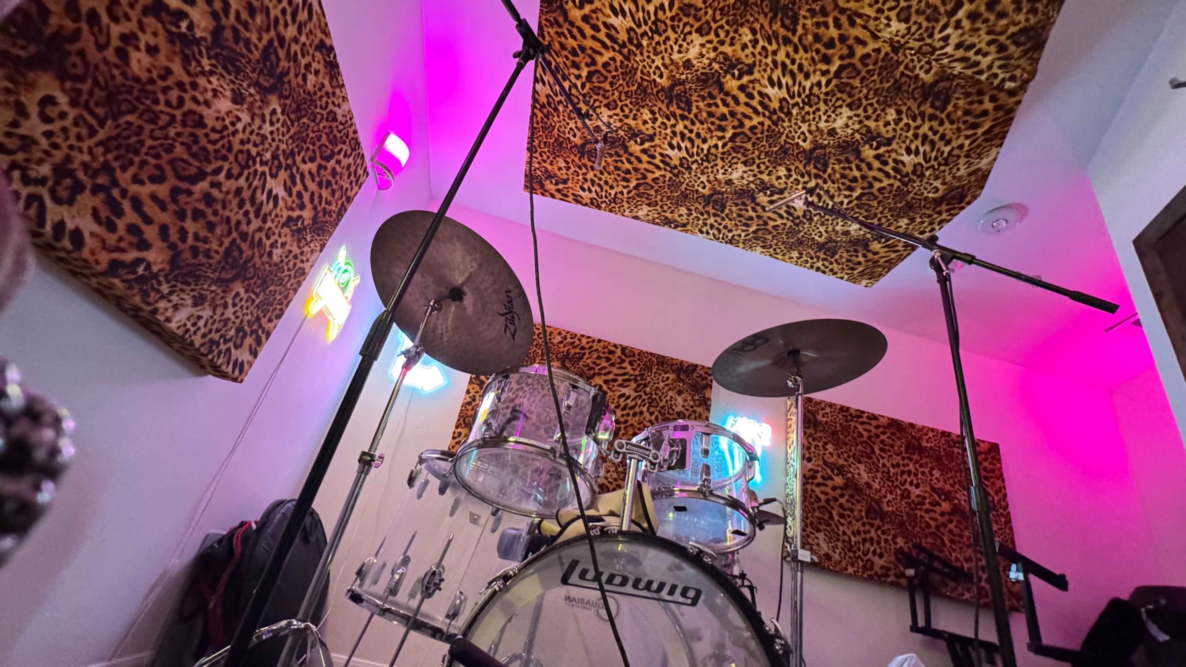 The image shows a drum set placed in a room with leopard print wall coverings and colorful lighting.