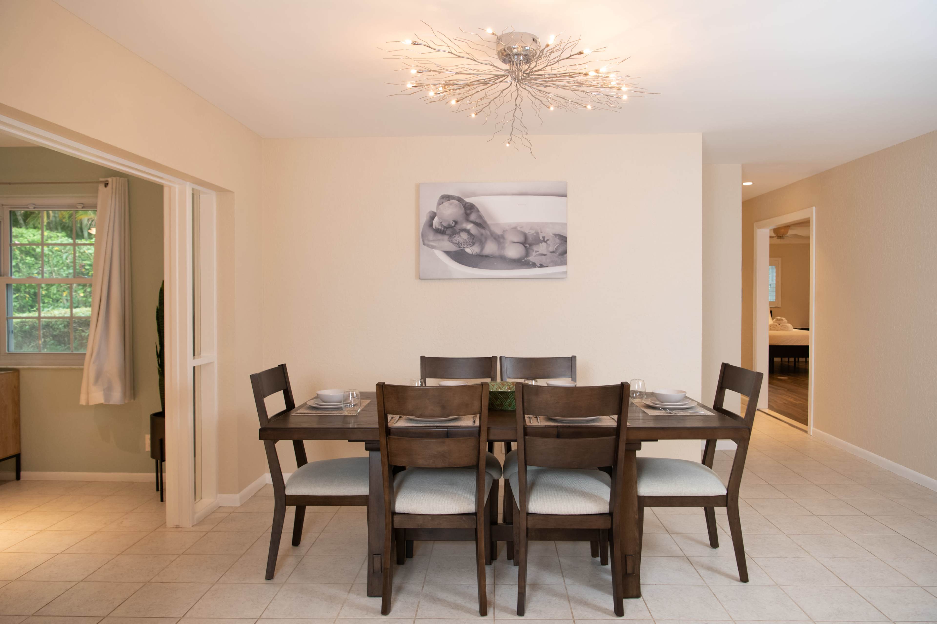 A dining area features a wooden table set for six, with a modern light fixture above and a black-and-white photograph on the wall.