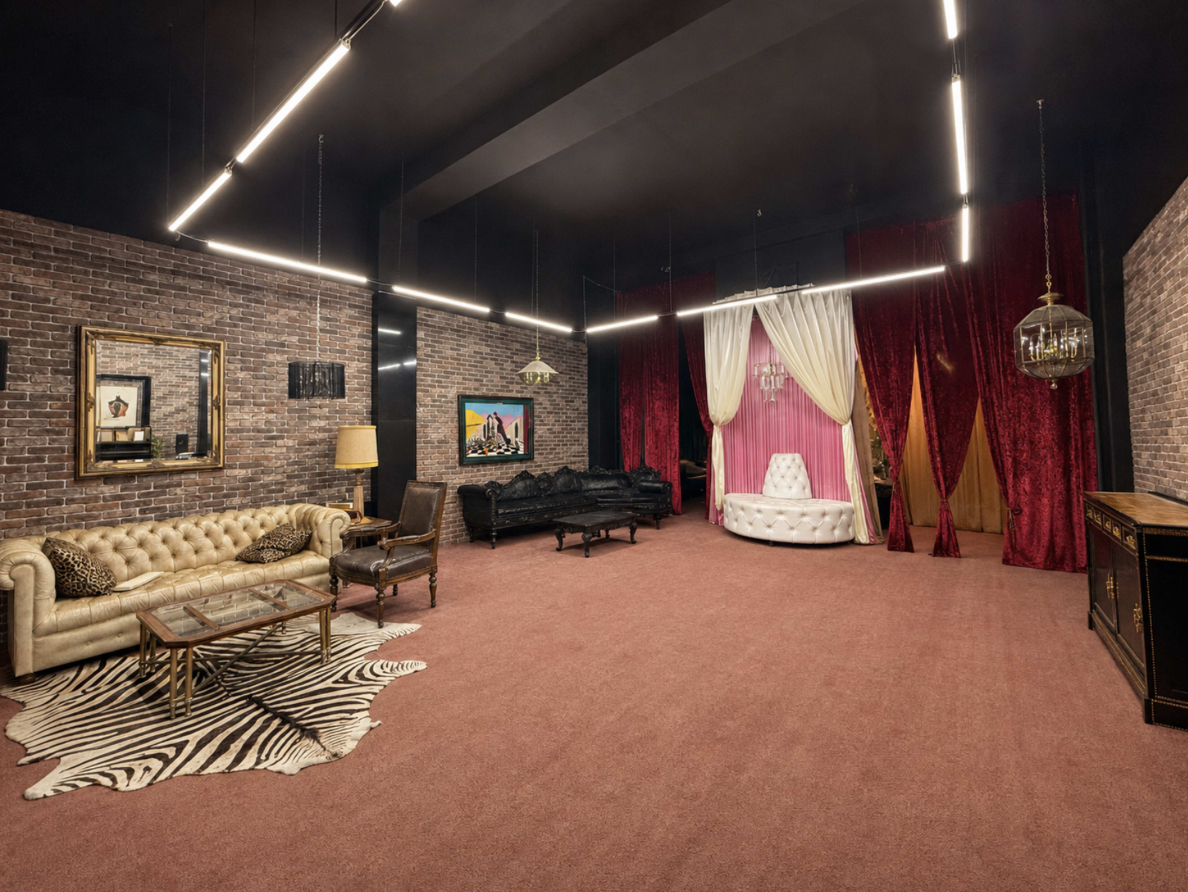 The room features a mix of furniture styles, including a beige tufted sofa, a black couch, and a white circular armchair, against a backdrop of brick walls and velvet curtains.