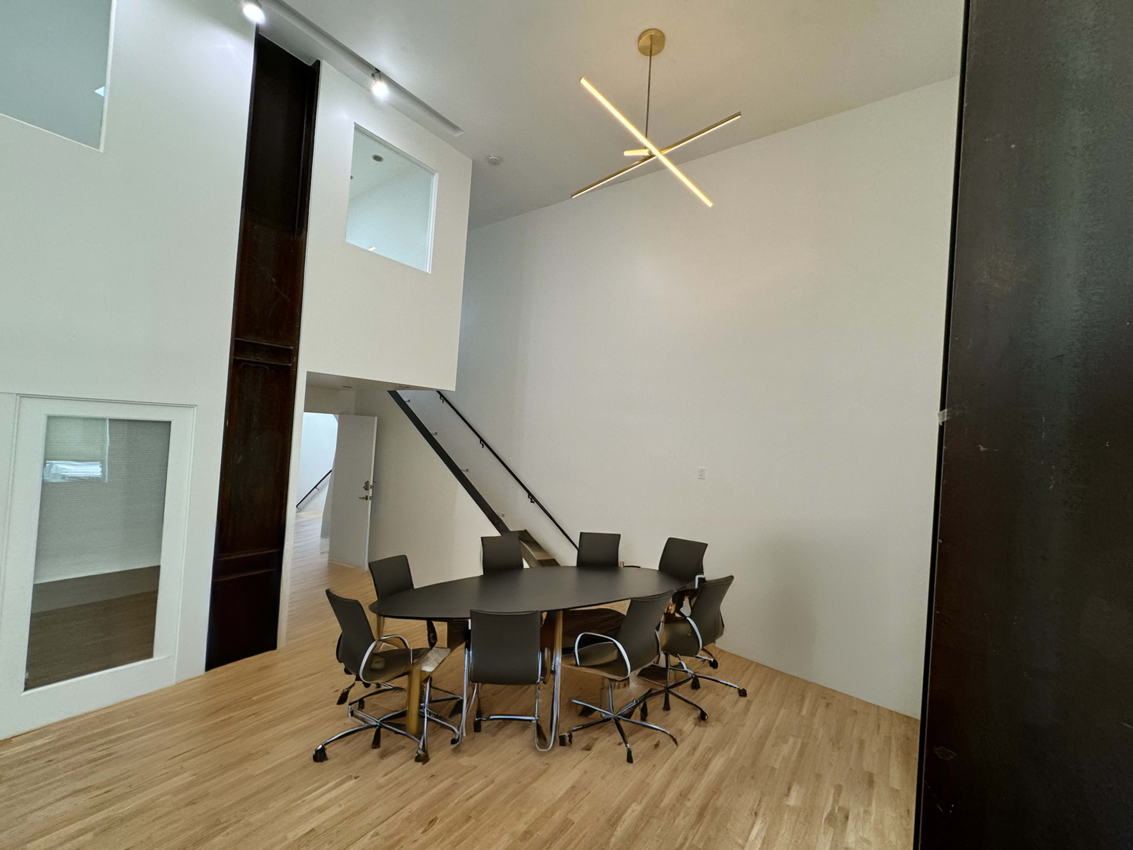 A modern meeting room features a round table surrounded by six chairs, with a staircase and large windows in the background.