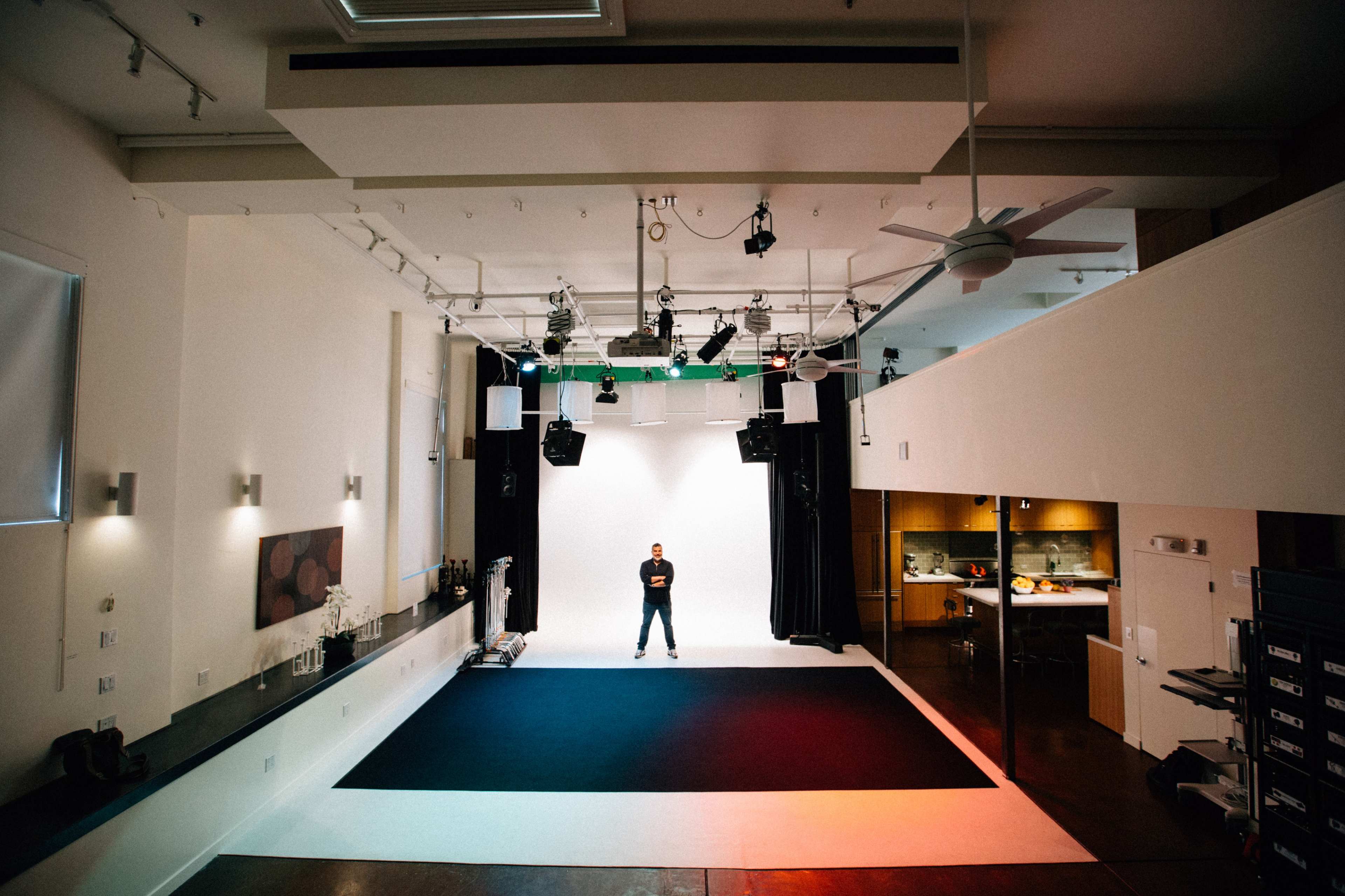 A person stands in the center of a spacious studio with white walls and a black and white floor.