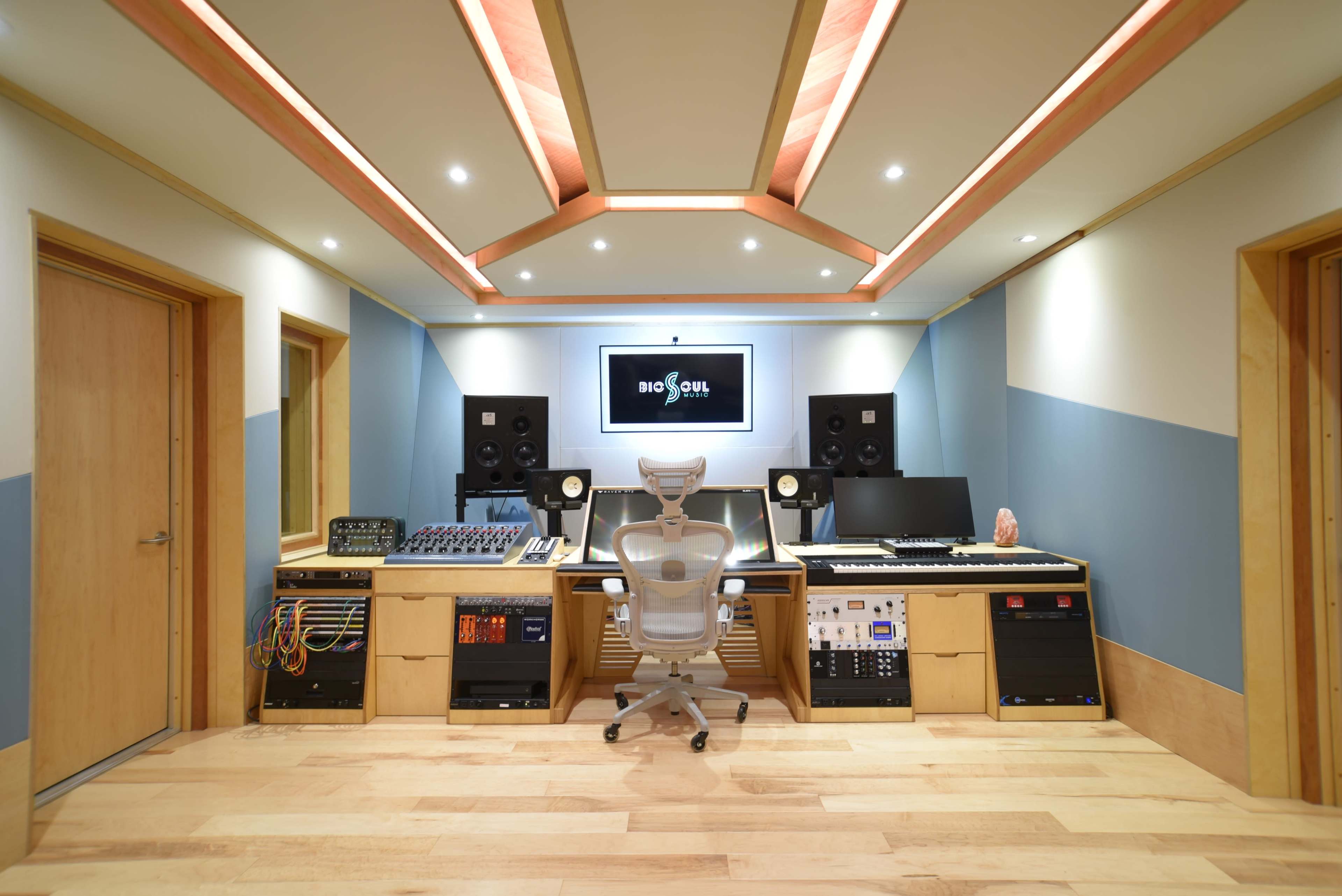 A music studio with a central desk, computer monitors, audio equipment, and soundproofing features.