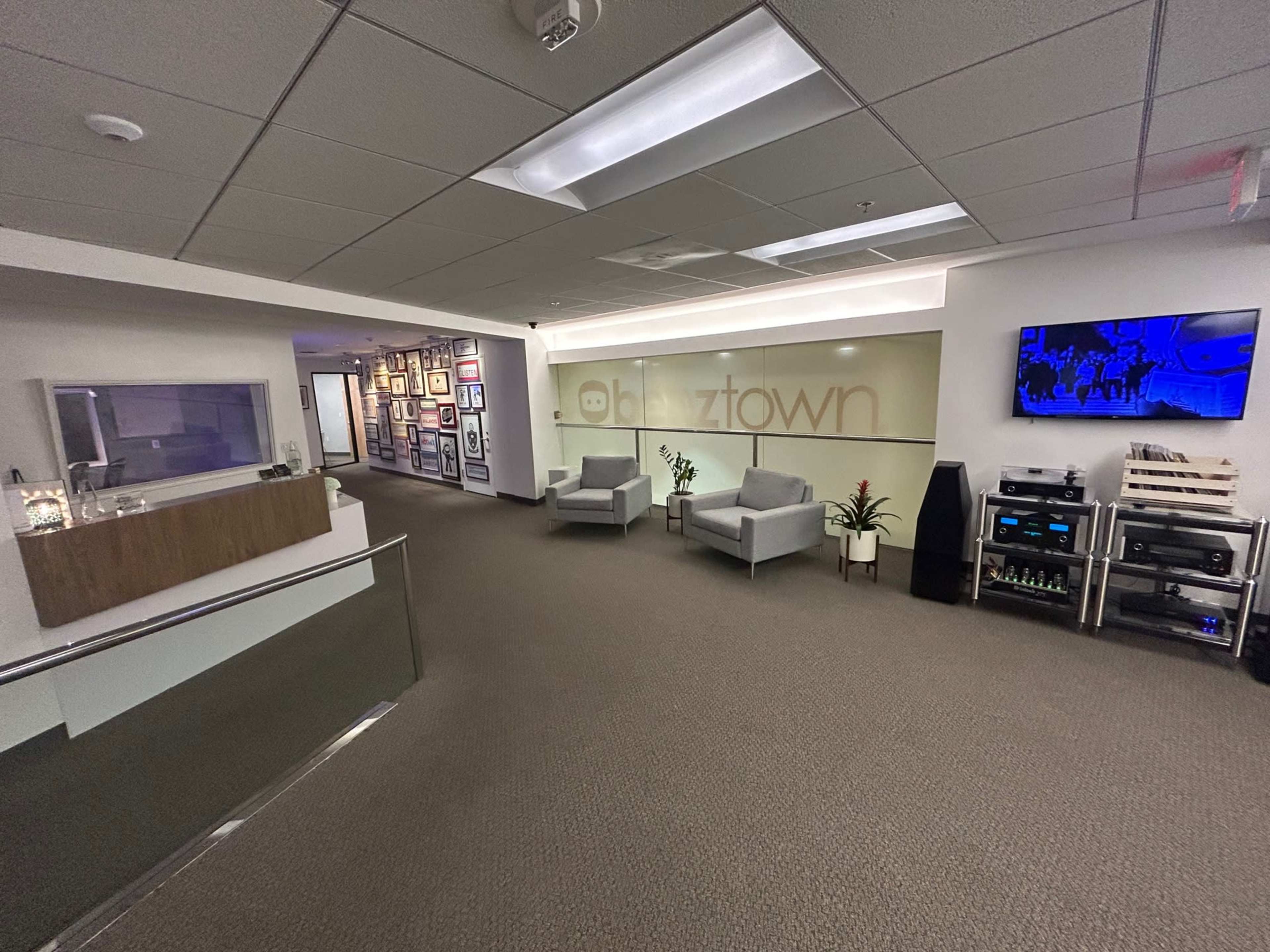 A modern office reception area with two gray armchairs, a decorative plant, and a wall featuring framed artwork.