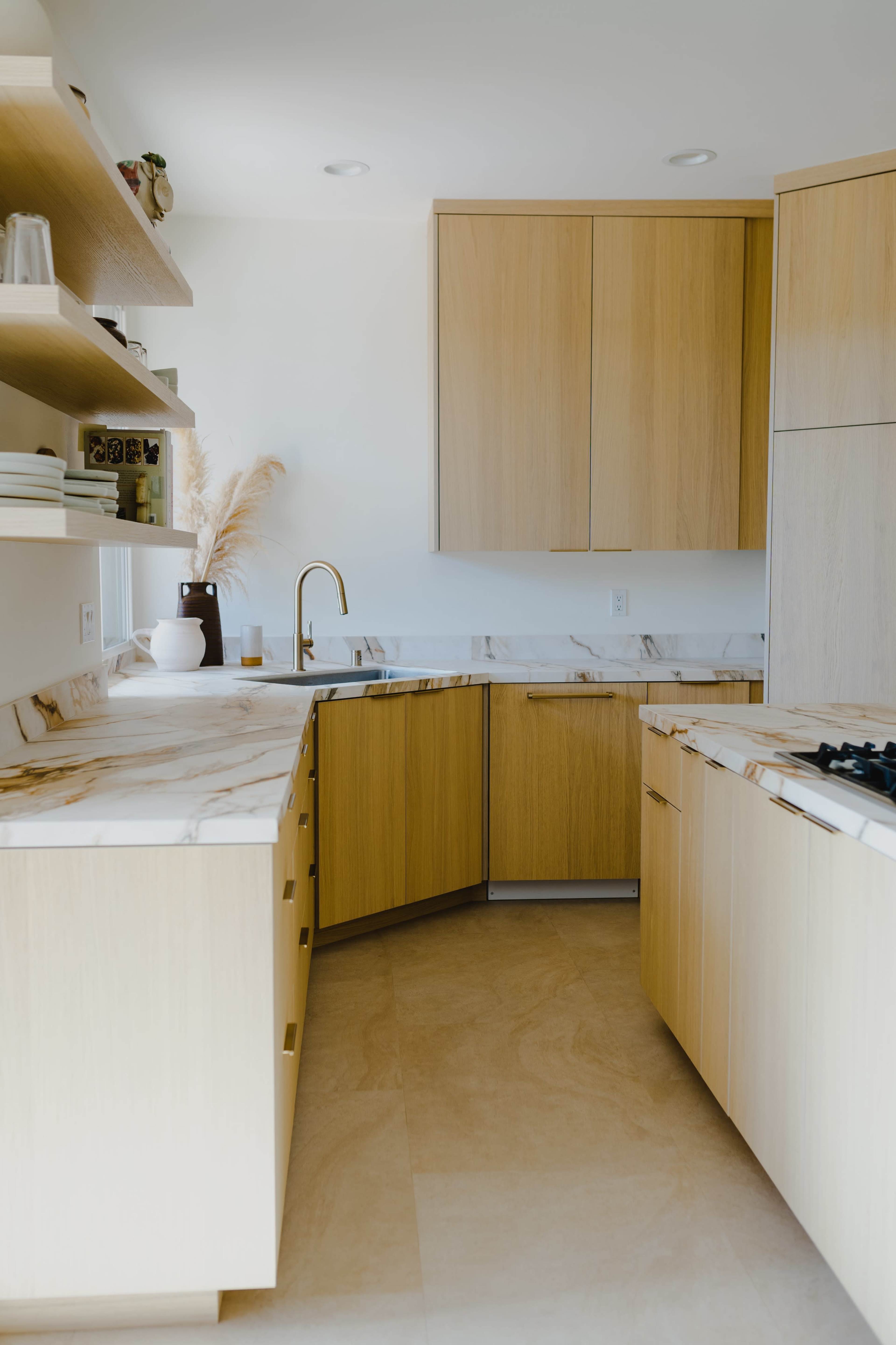 A modern kitchen features light wooden cabinetry, white marble countertops, and minimalistic decor.