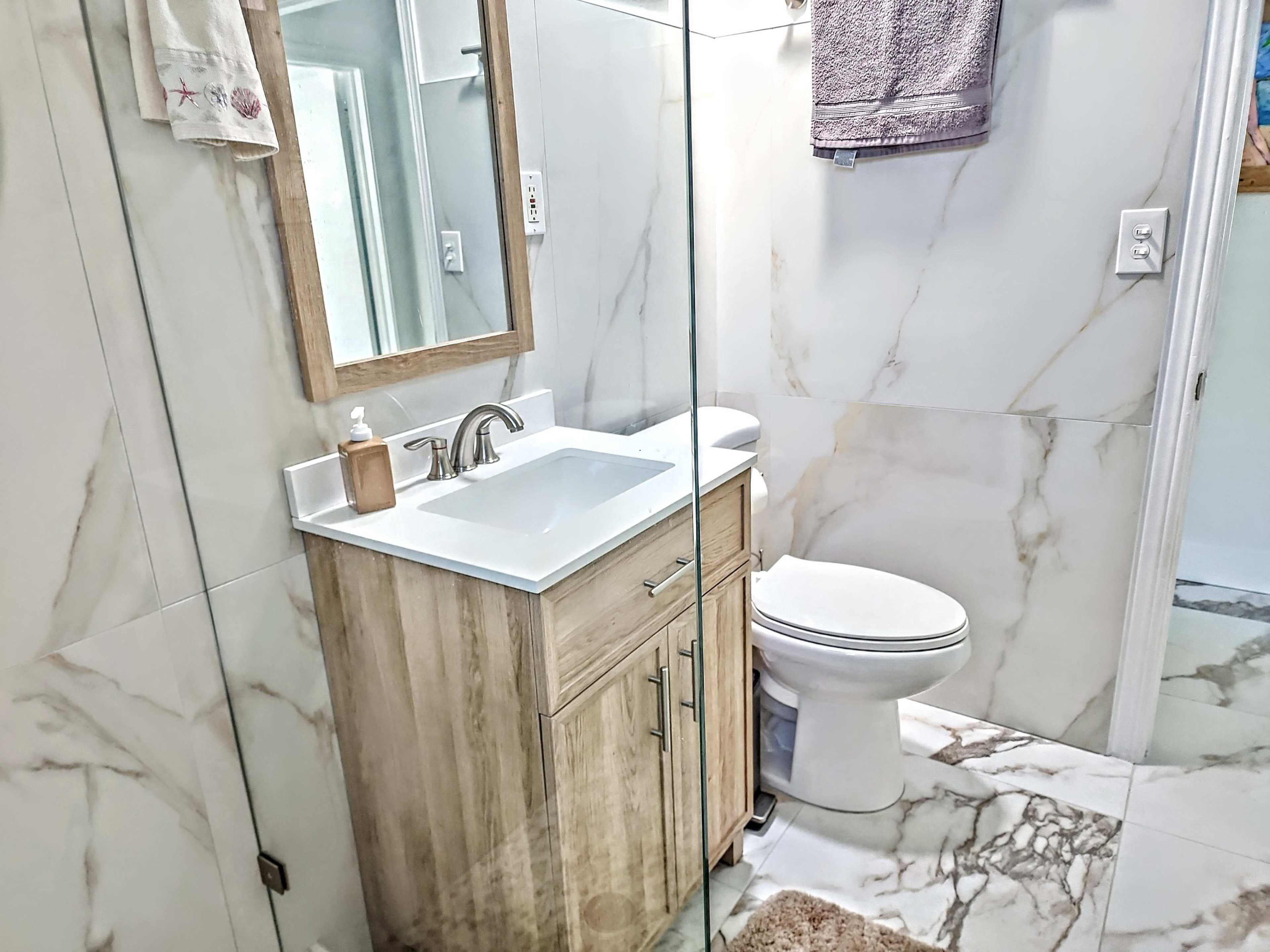 A modern bathroom featuring a wooden vanity with a white sink, a mirror, a toilet, and marble-patterned tiles.