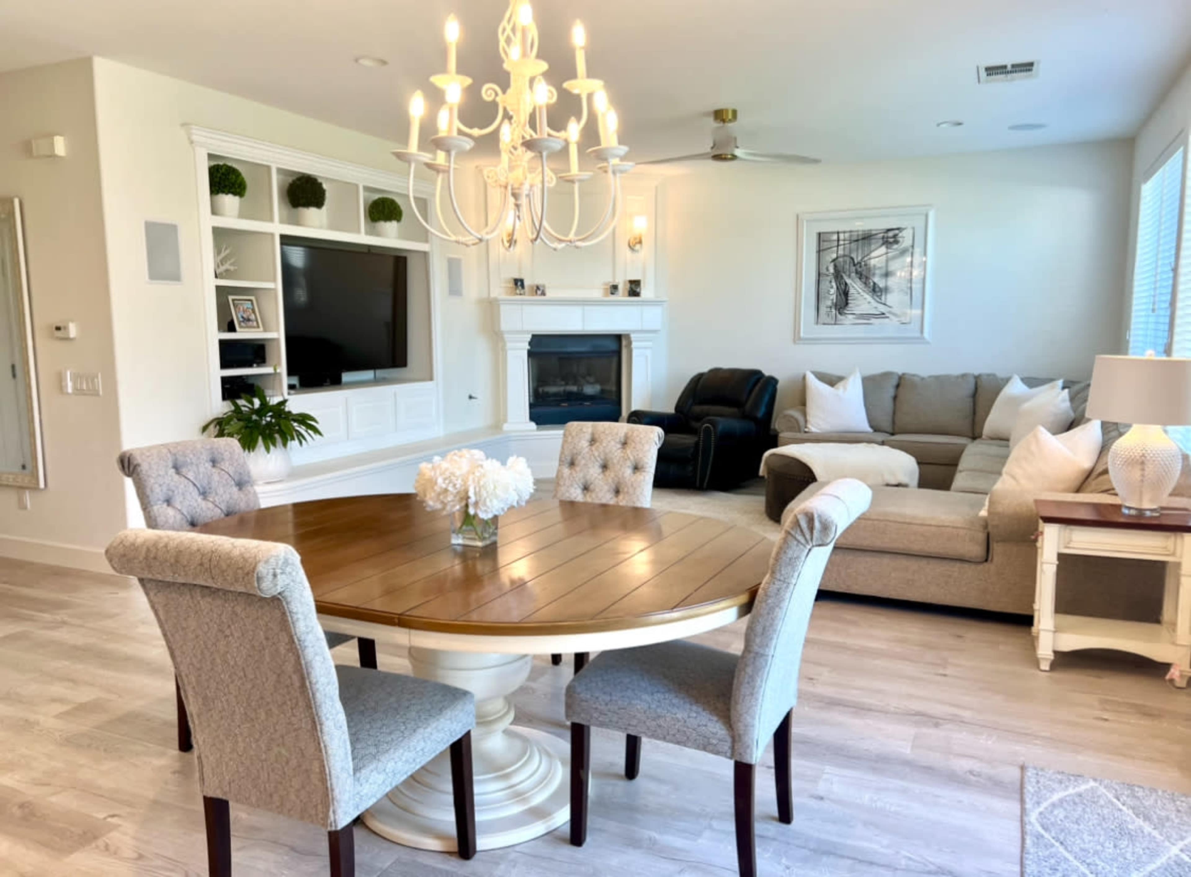 A modern living room with a circular wooden dining table surrounded by four upholstered chairs, a sofa, a fireplace, and a wall-mounted television.