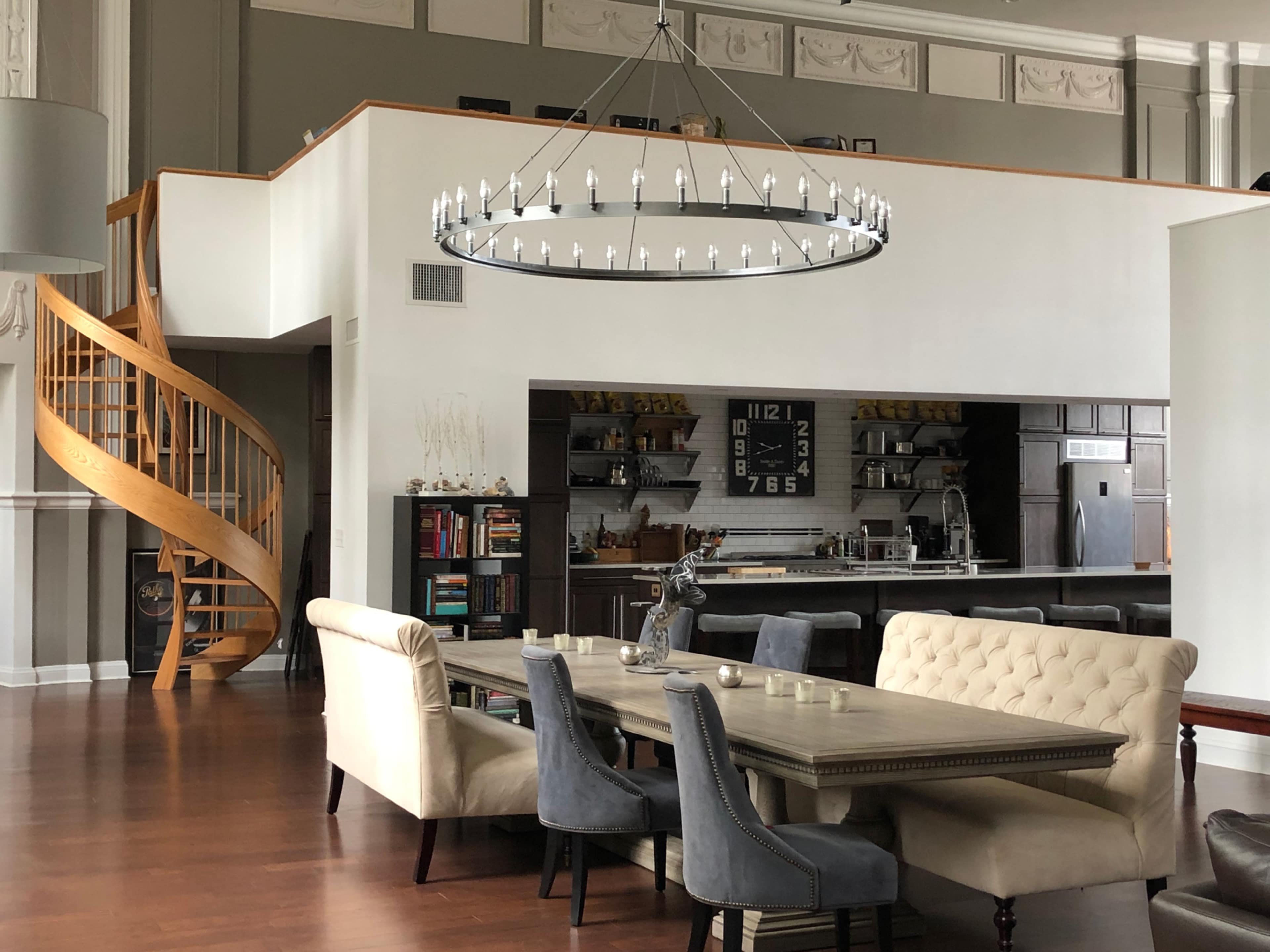 A modern open-concept living space featuring a dining area with a large table, a spiral staircase, and a well-equipped kitchen in the background.