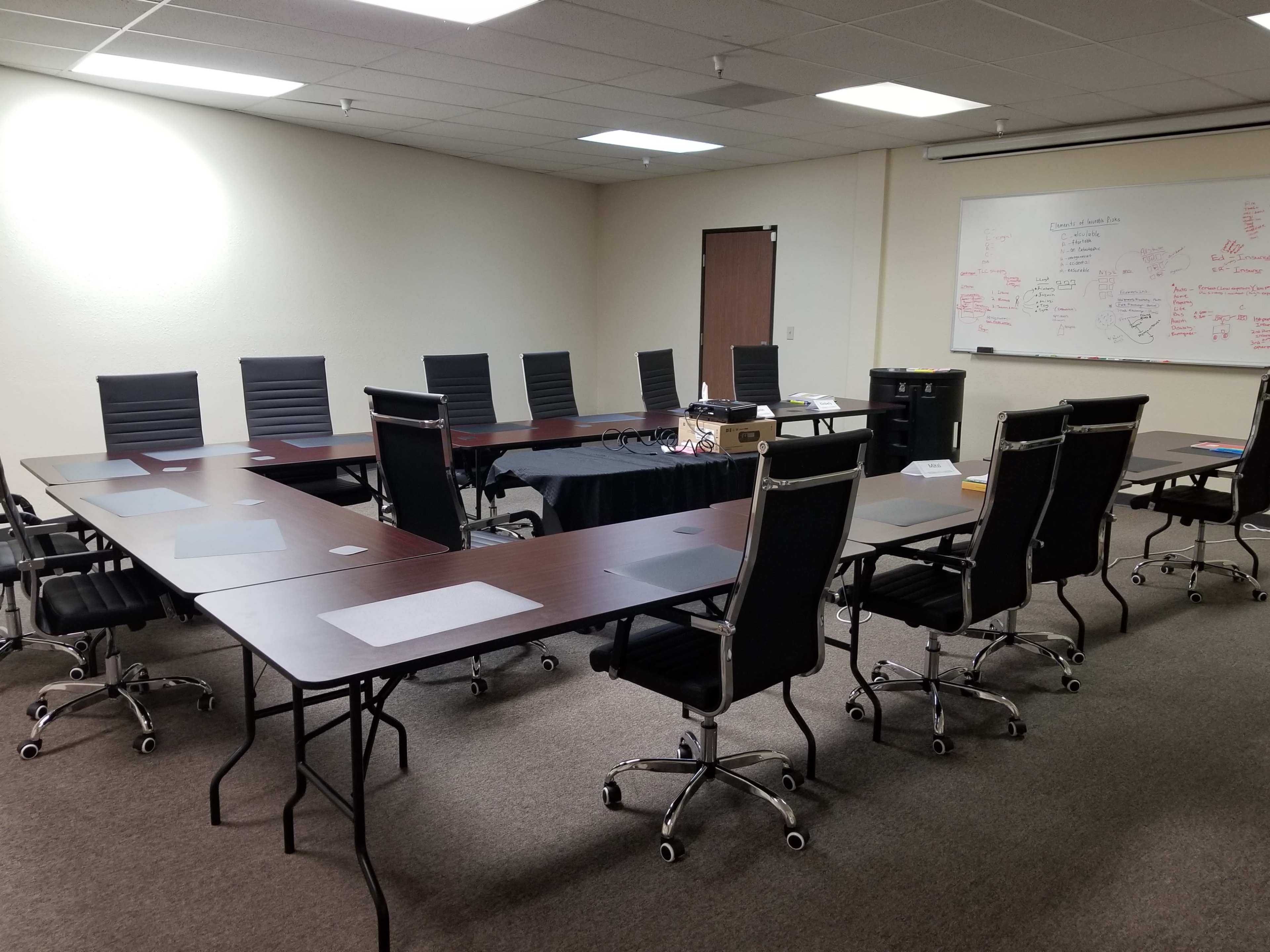 A conference room with a large oval table surrounded by several black office chairs and a whiteboard covered in notes on the wall.