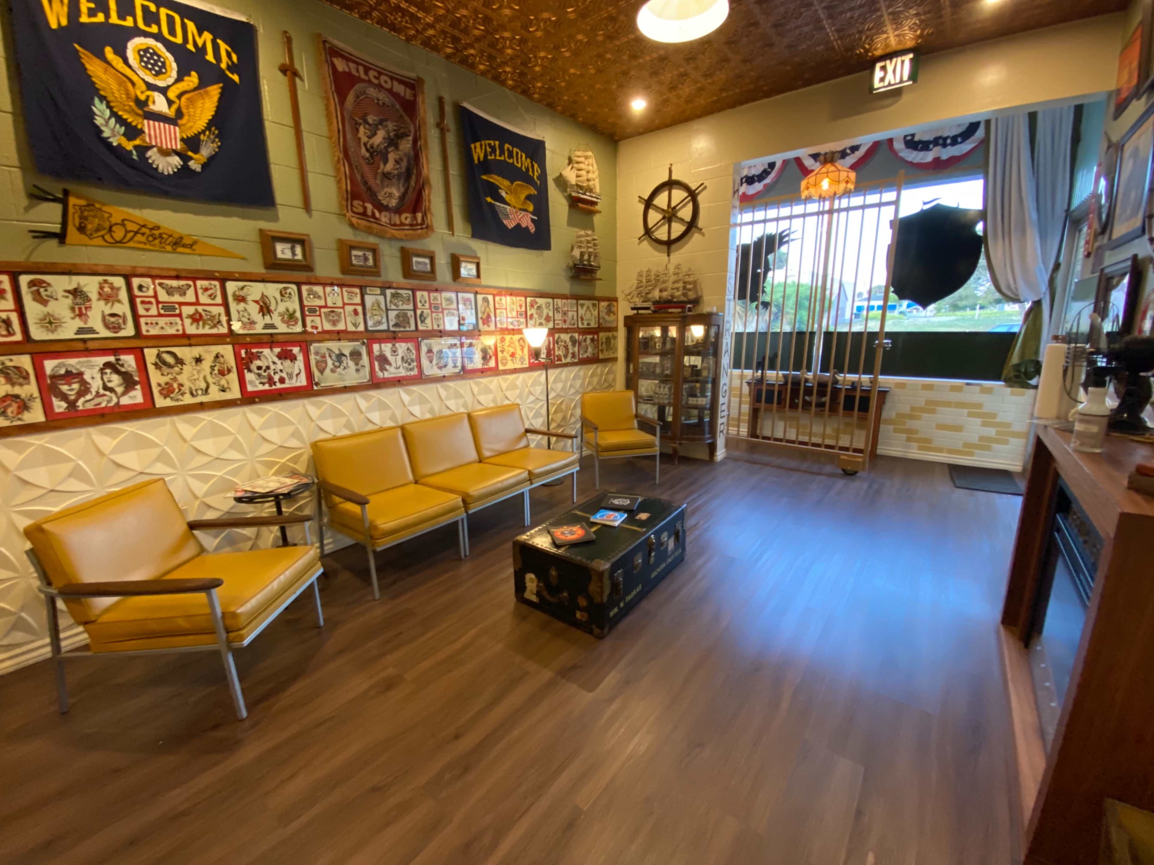 The interior of the room features a seating area with yellow chairs and a wooden coffee table, surrounded by framed art and decorative flags.