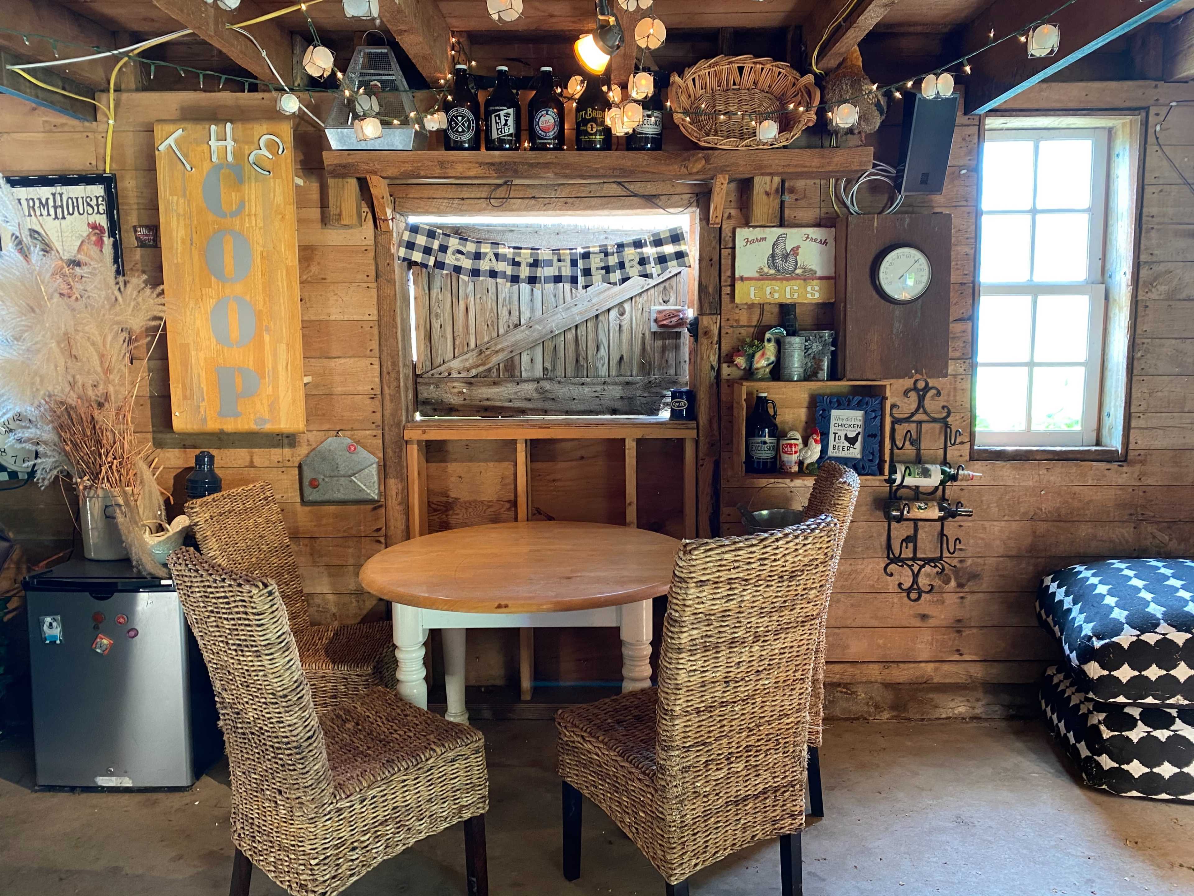 A cozy interior of a rustic shed featuring a round table with two wicker chairs, decorated walls, and various items on display.