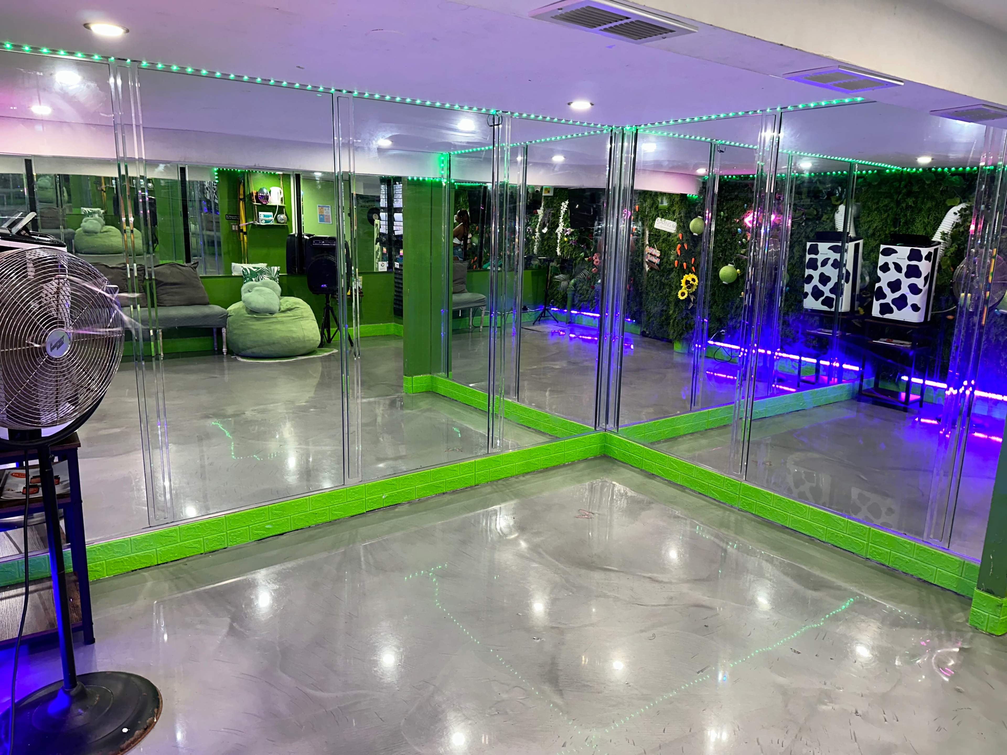 A room with mirrored walls, green accents, and colorful lighting, featuring seating areas and indoor plants.