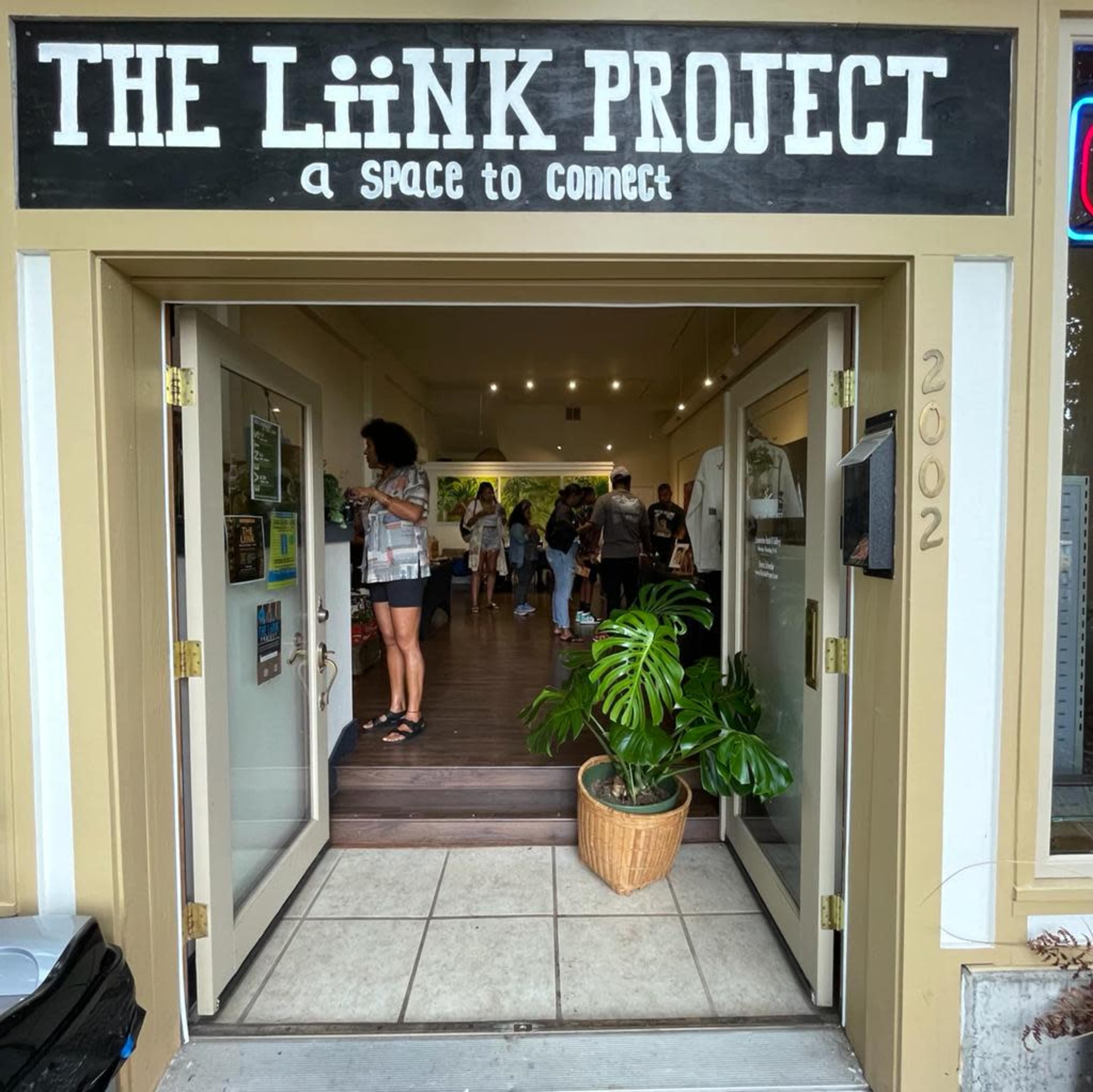 The entrance of "The Liink Project," a communal space with people inside and a potted plant by the door.