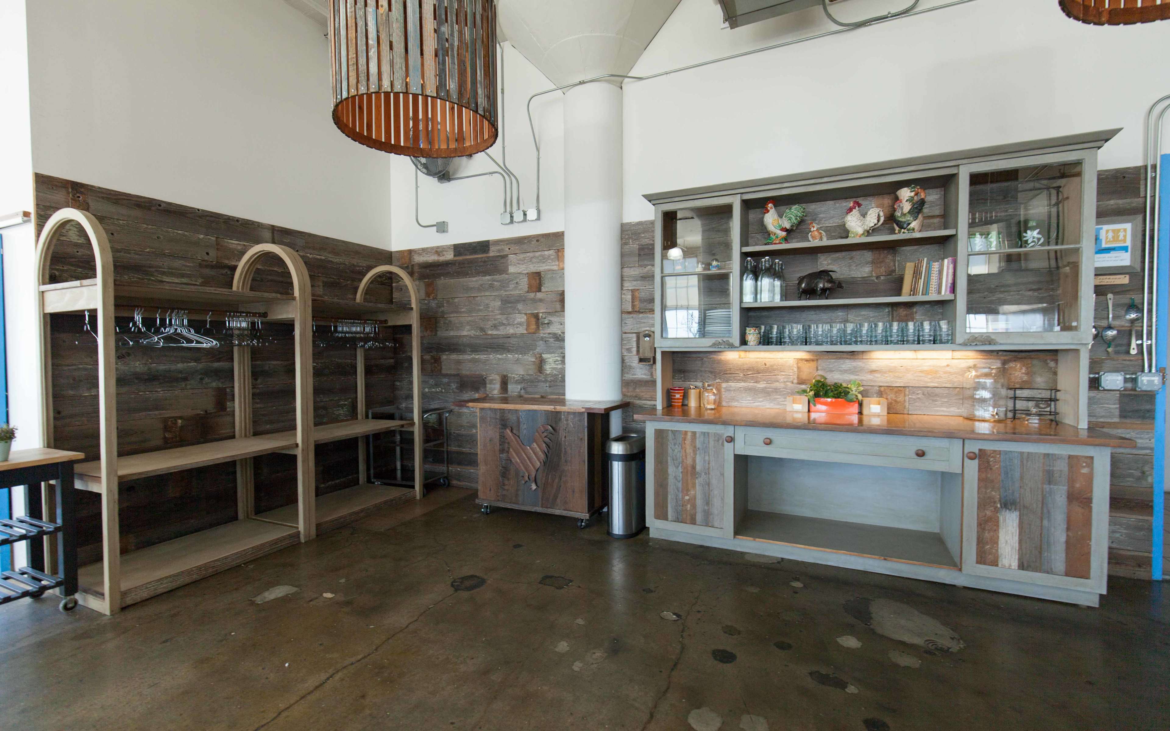 A spacious interior with wooden shelving units, a cabinet with glass shelves, and a counter area, all set against a backdrop of textured wooden walls.
