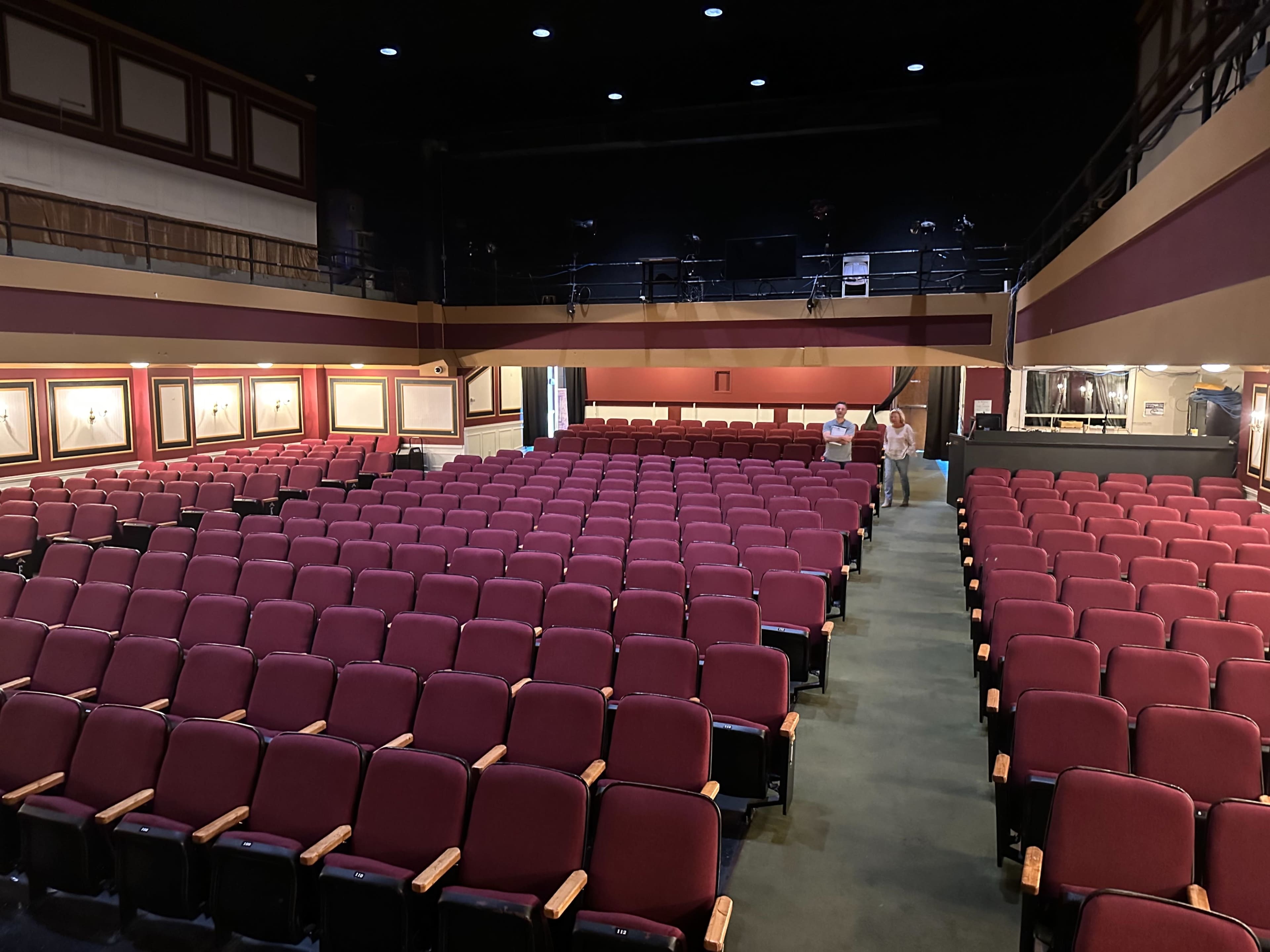 The image shows an empty theater with rows of maroon seats facing a dark stage area.