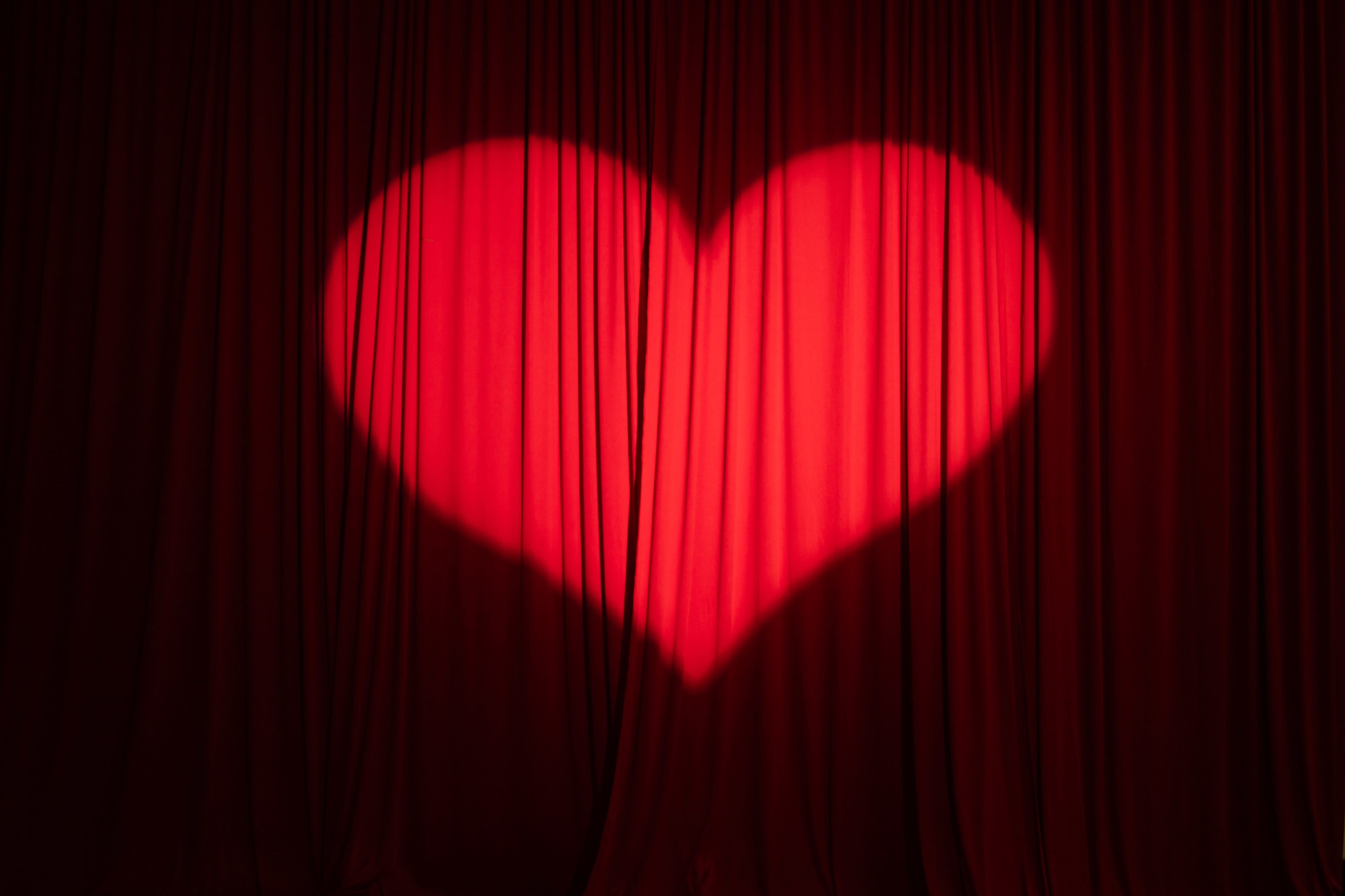 A red heart is illuminated on a backdrop of flowing red curtains.