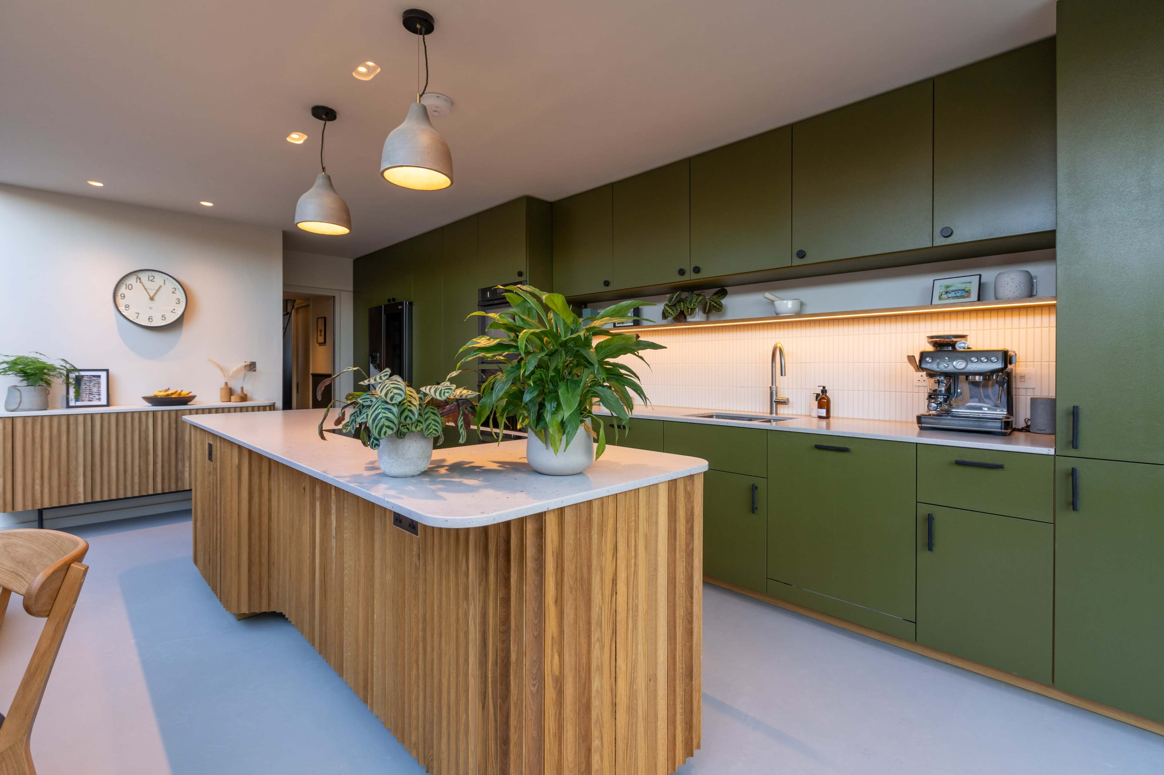 The image shows a modern kitchen featuring green cabinetry, a wooden island, and stylish pendant lighting.